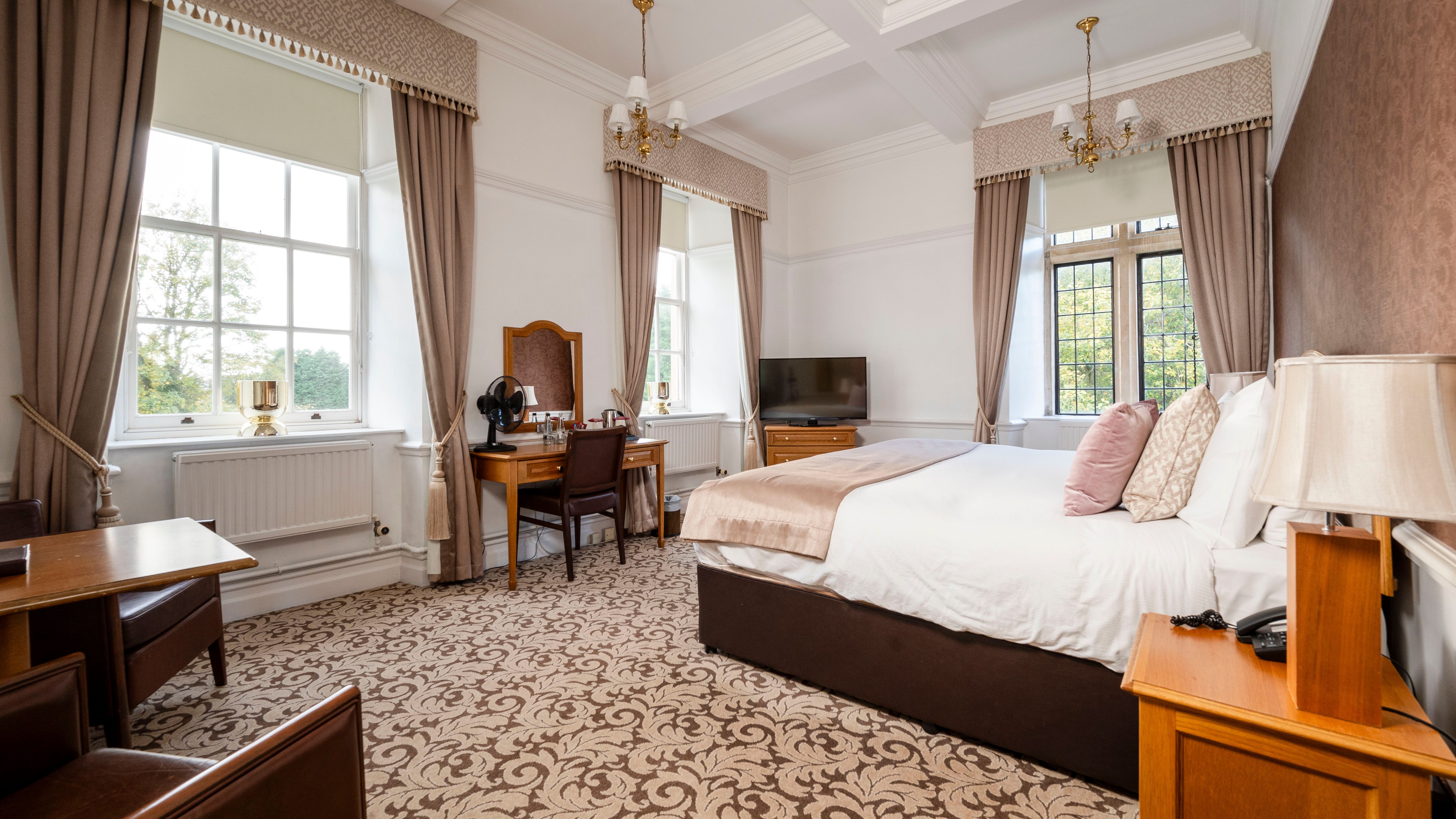 Bright and spacious hotel room with a large bed, elegant curtains, a desk, and a TV.