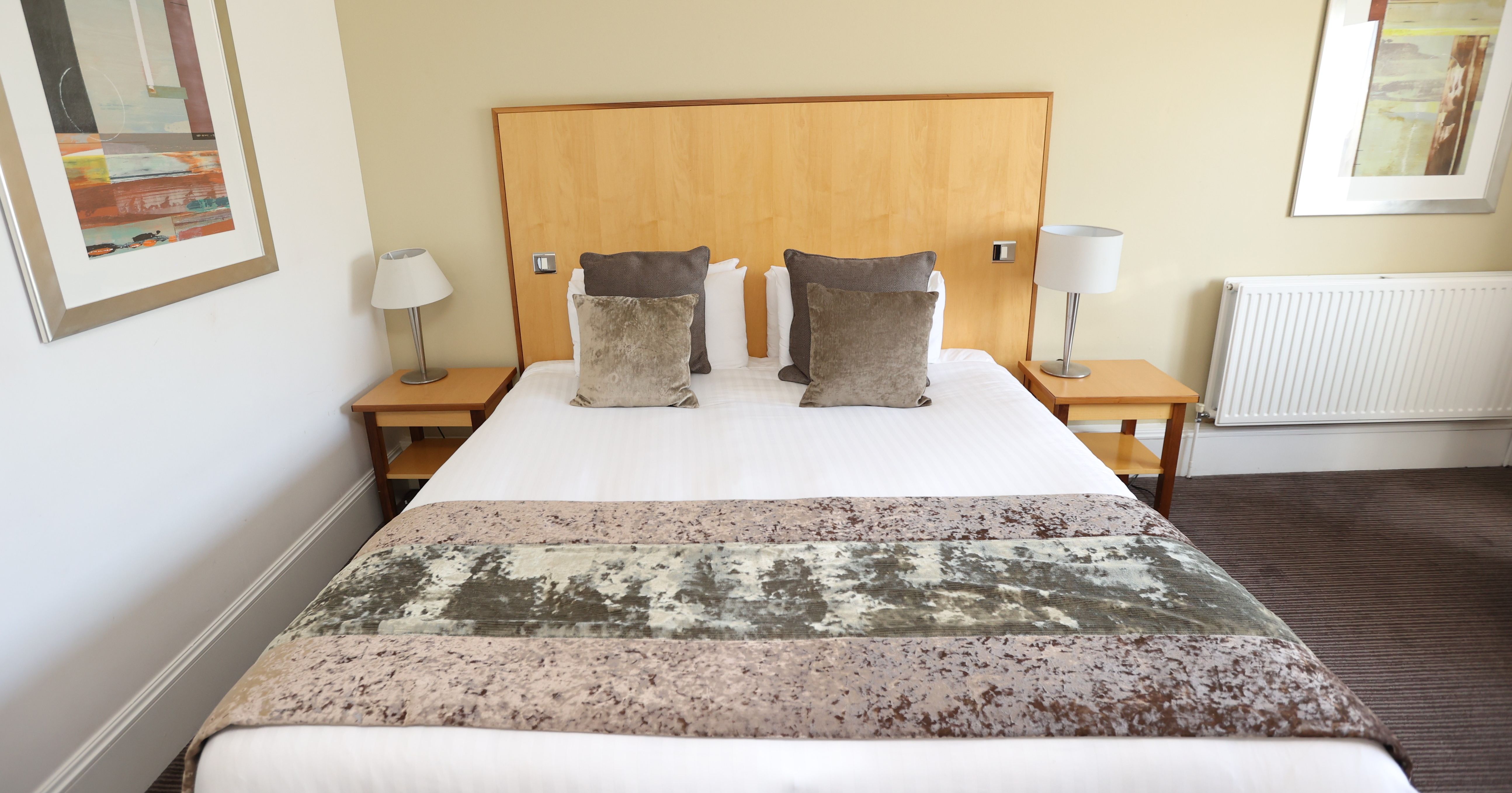 A modern hotel room with a double bed, two nightstands, and abstract art on the walls.