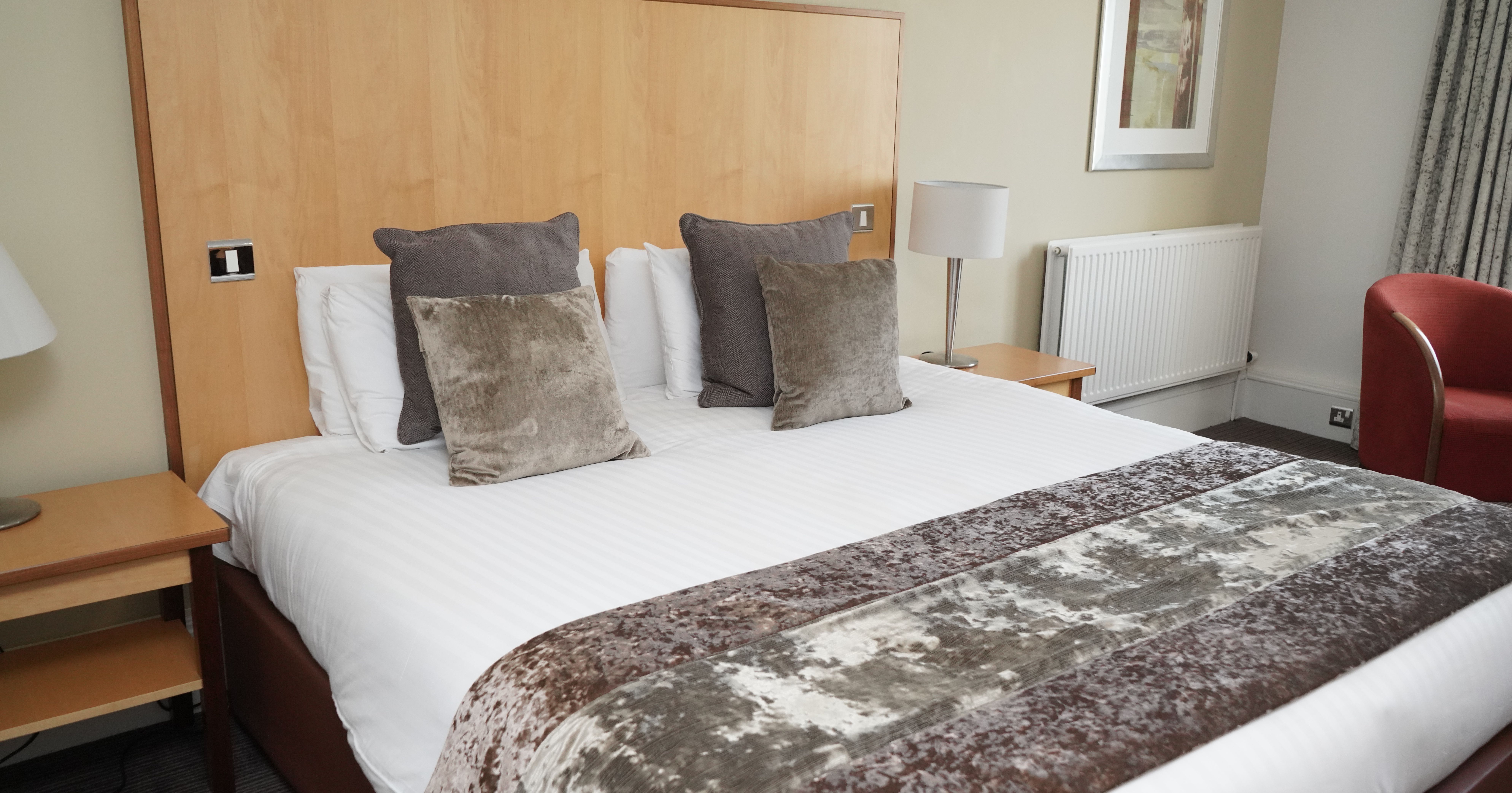 Neatly made hotel bed with decorative pillows and a plush runner