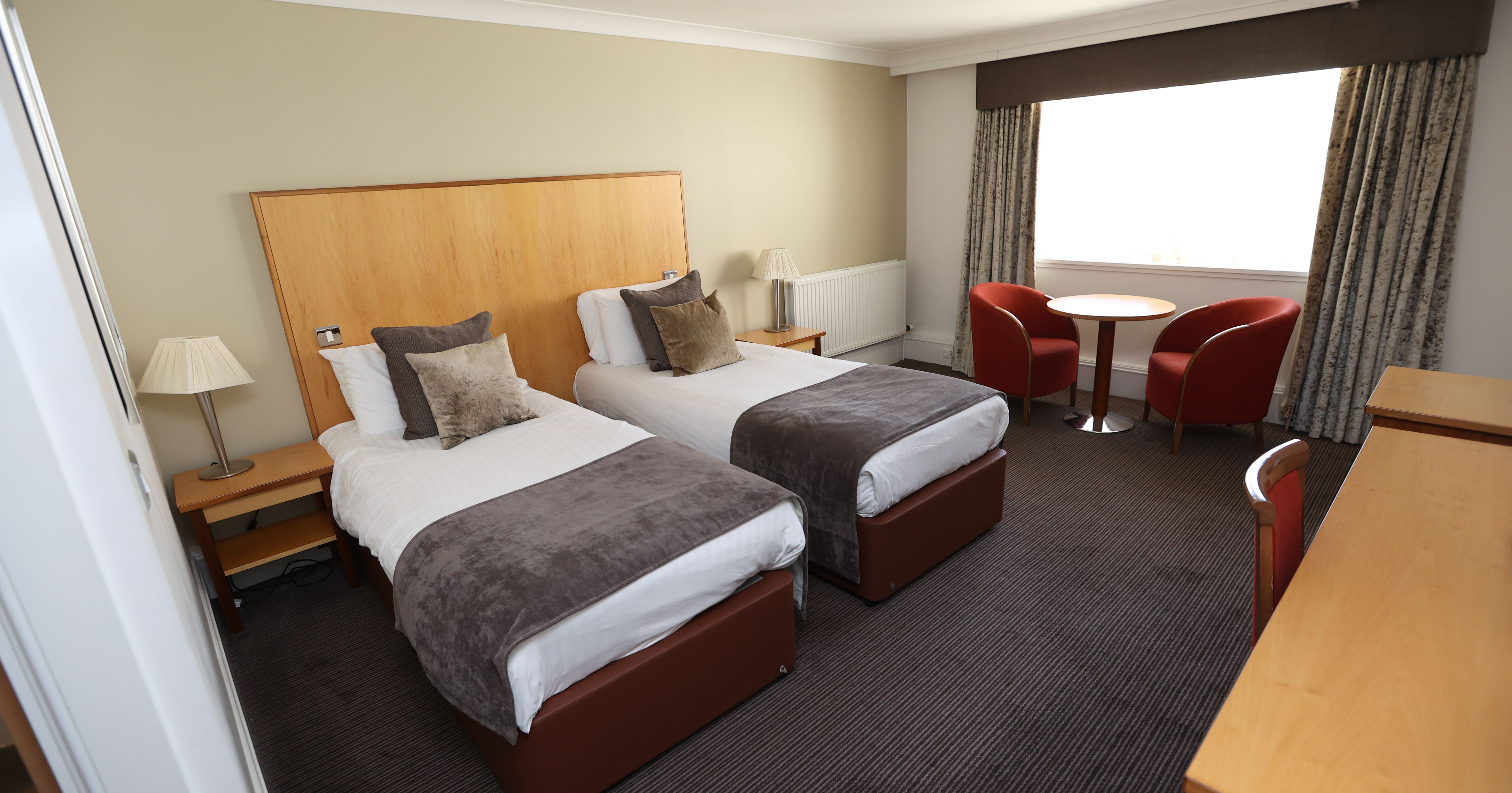 Modern hotel room with two single beds, chairs, desk, and large window