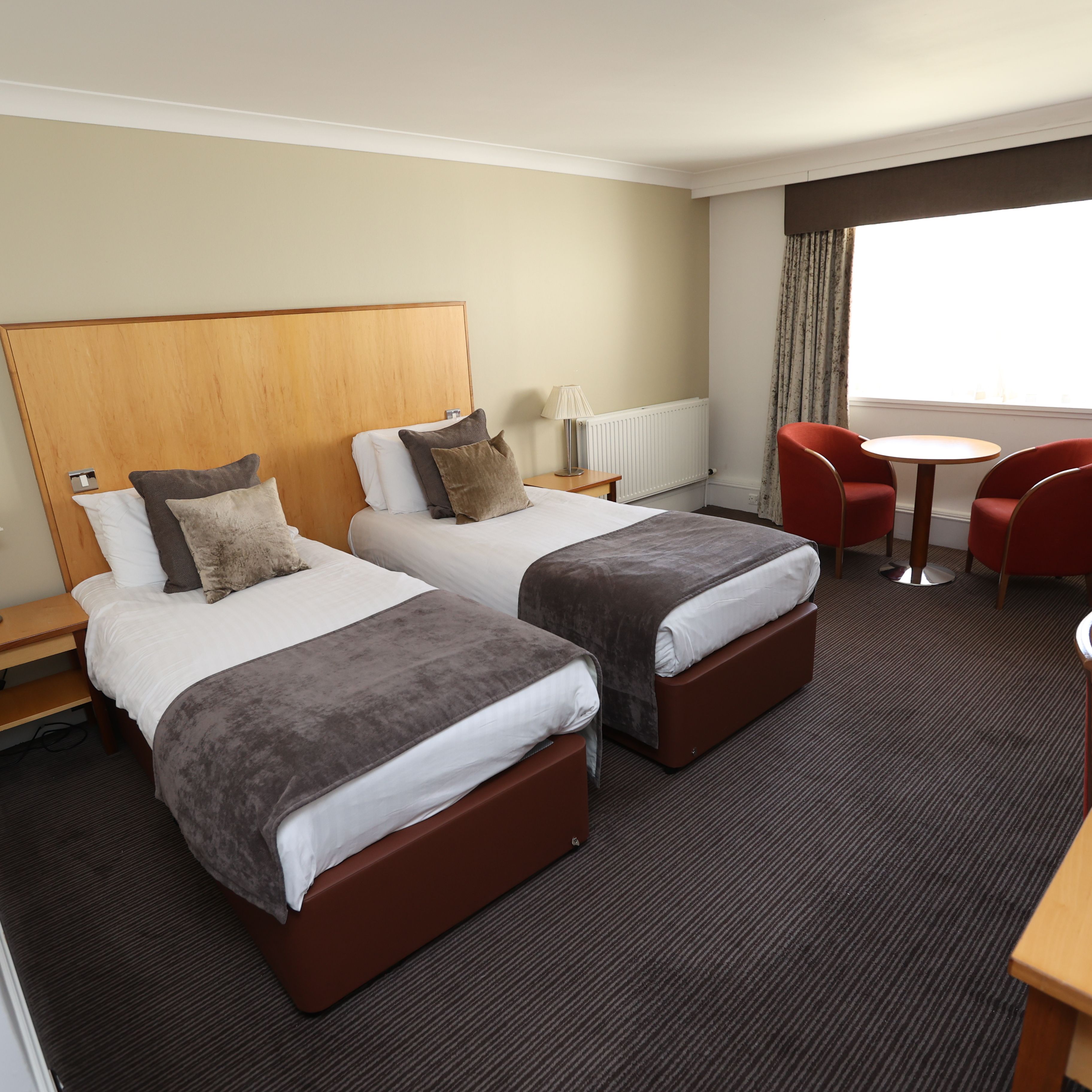 Modern hotel room with two single beds, chairs, desk, and large window