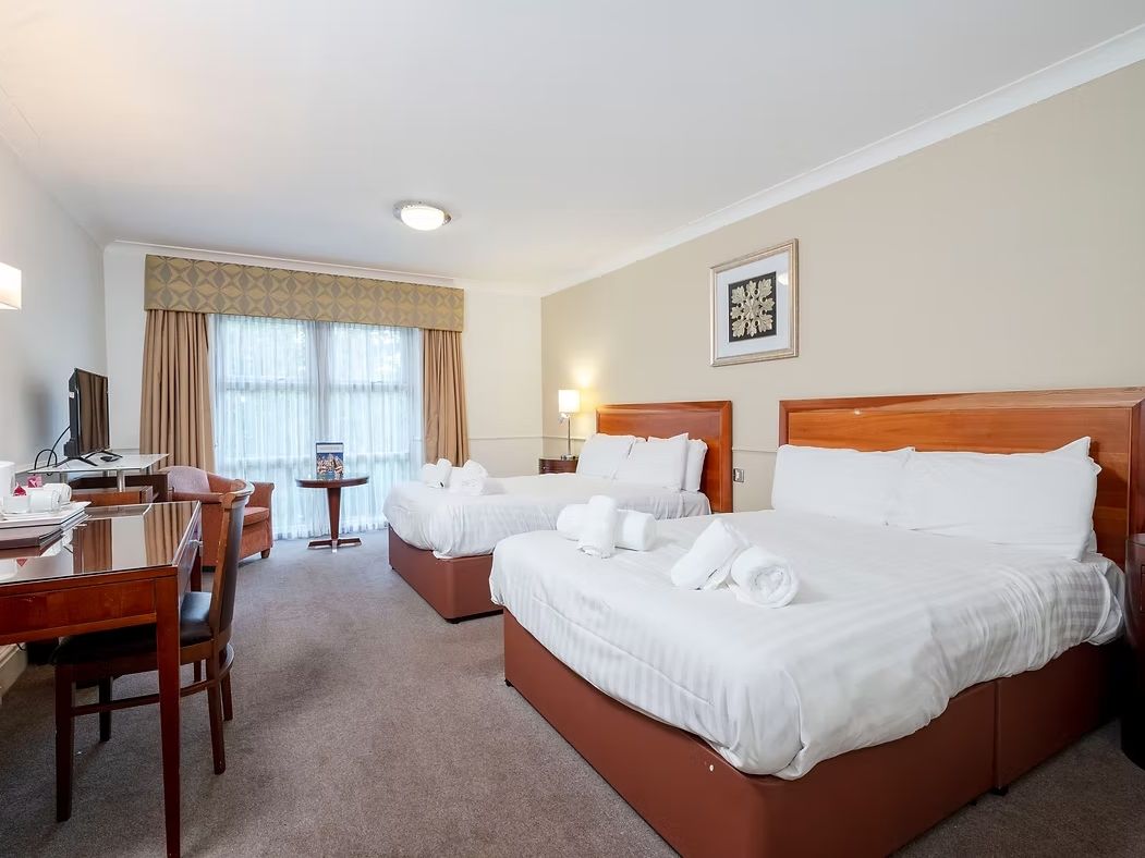 Hotel room with two double beds, work desk, television, and large window.