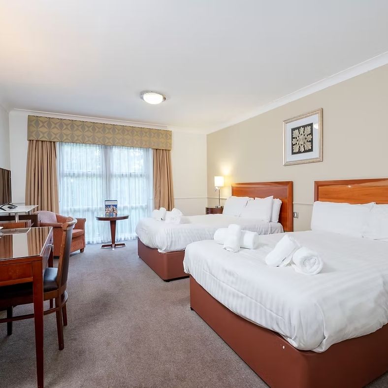 Hotel room with two double beds, work desk, television, and large window.