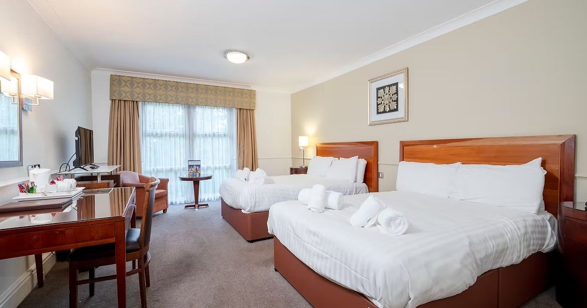 Hotel room with two double beds, work desk, television, and large window.