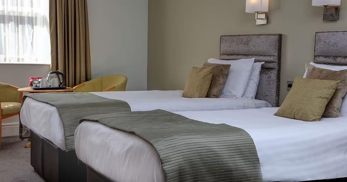 Modern hotel room with two single beds, soft lighting, and a table with tea and coffee set.