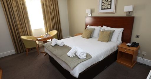 Neatly arranged hotel room with a double bed, bedside tables, and a small seating area by the window.