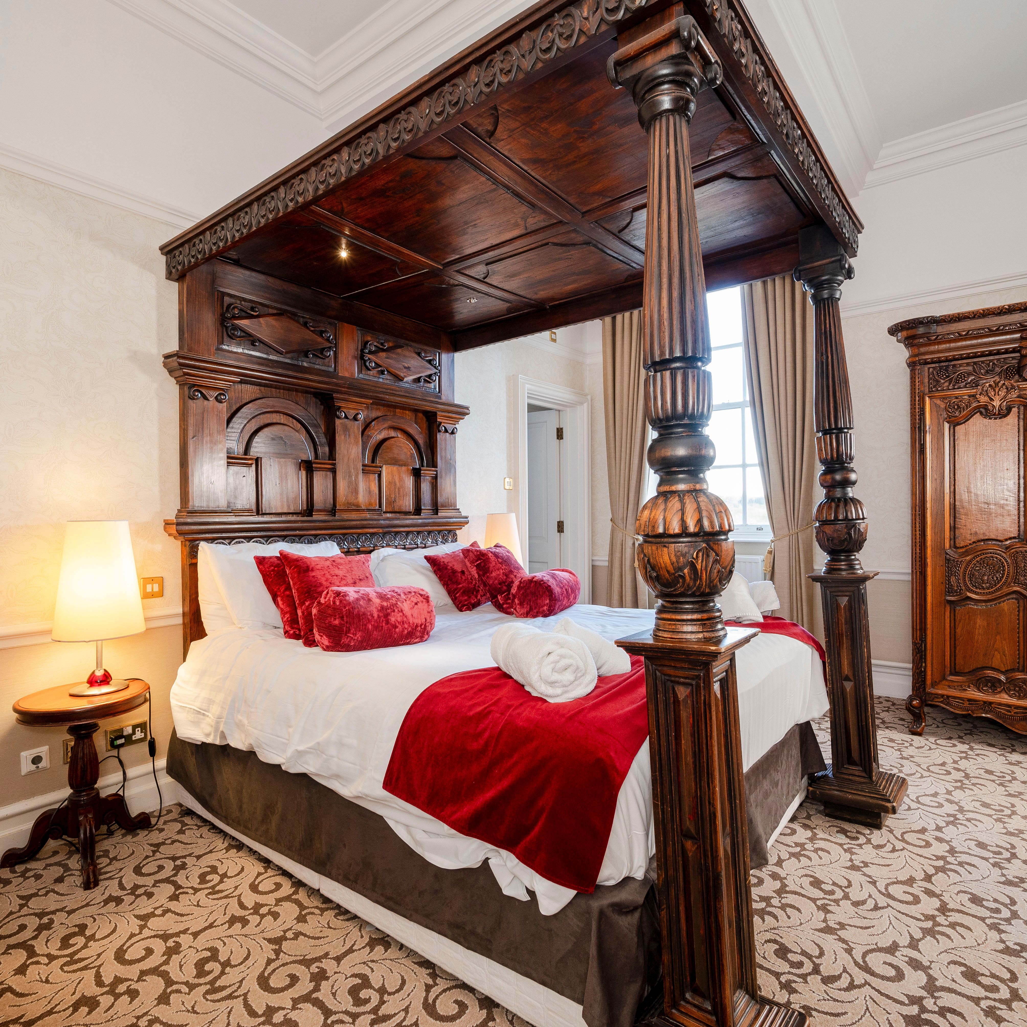 Luxurious bedroom with a large ornate wooden canopy bed, red accents, and antique furniture