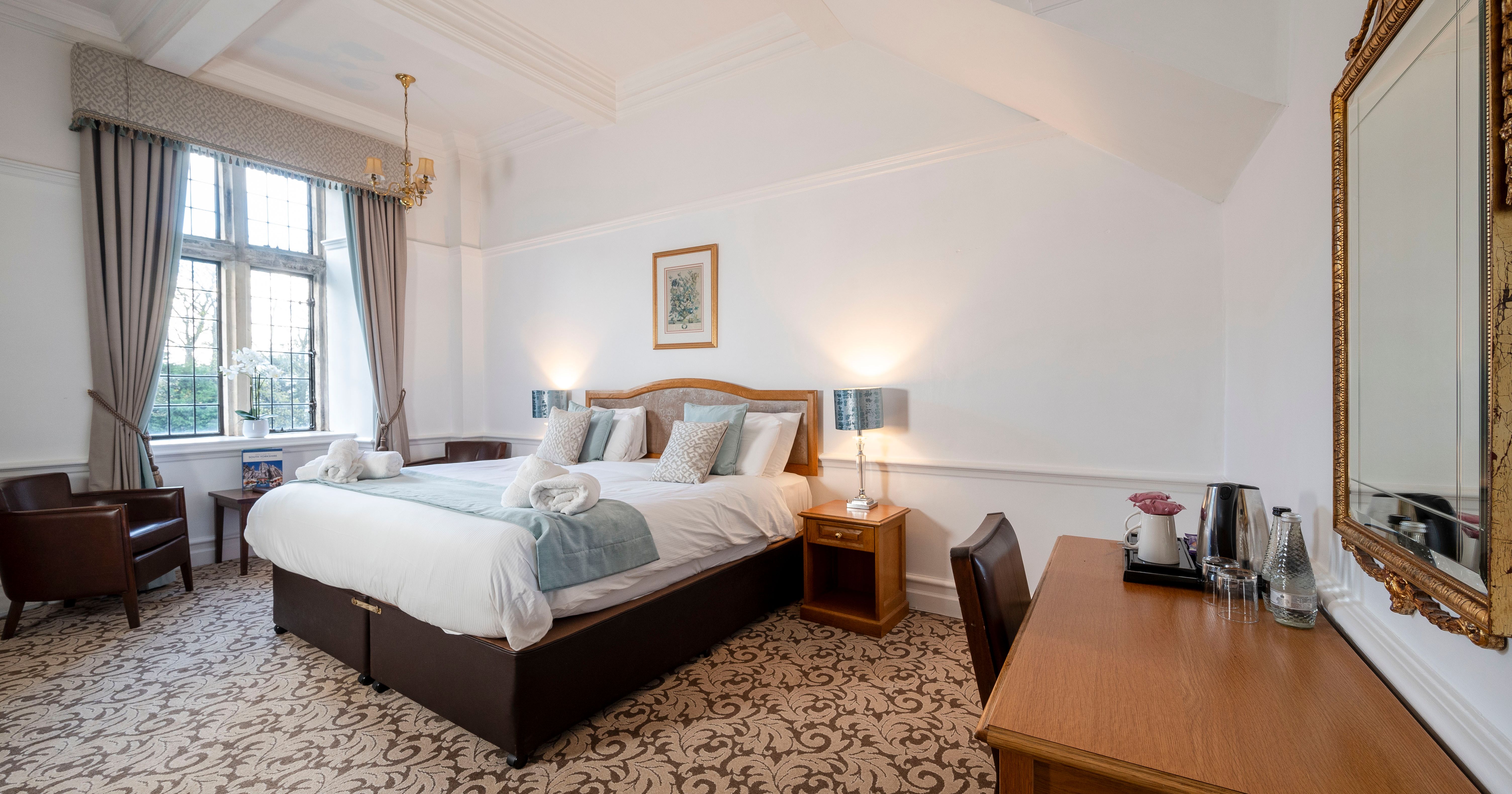 Elegant hotel room with a large bed, wooden furniture, and a window with curtains.