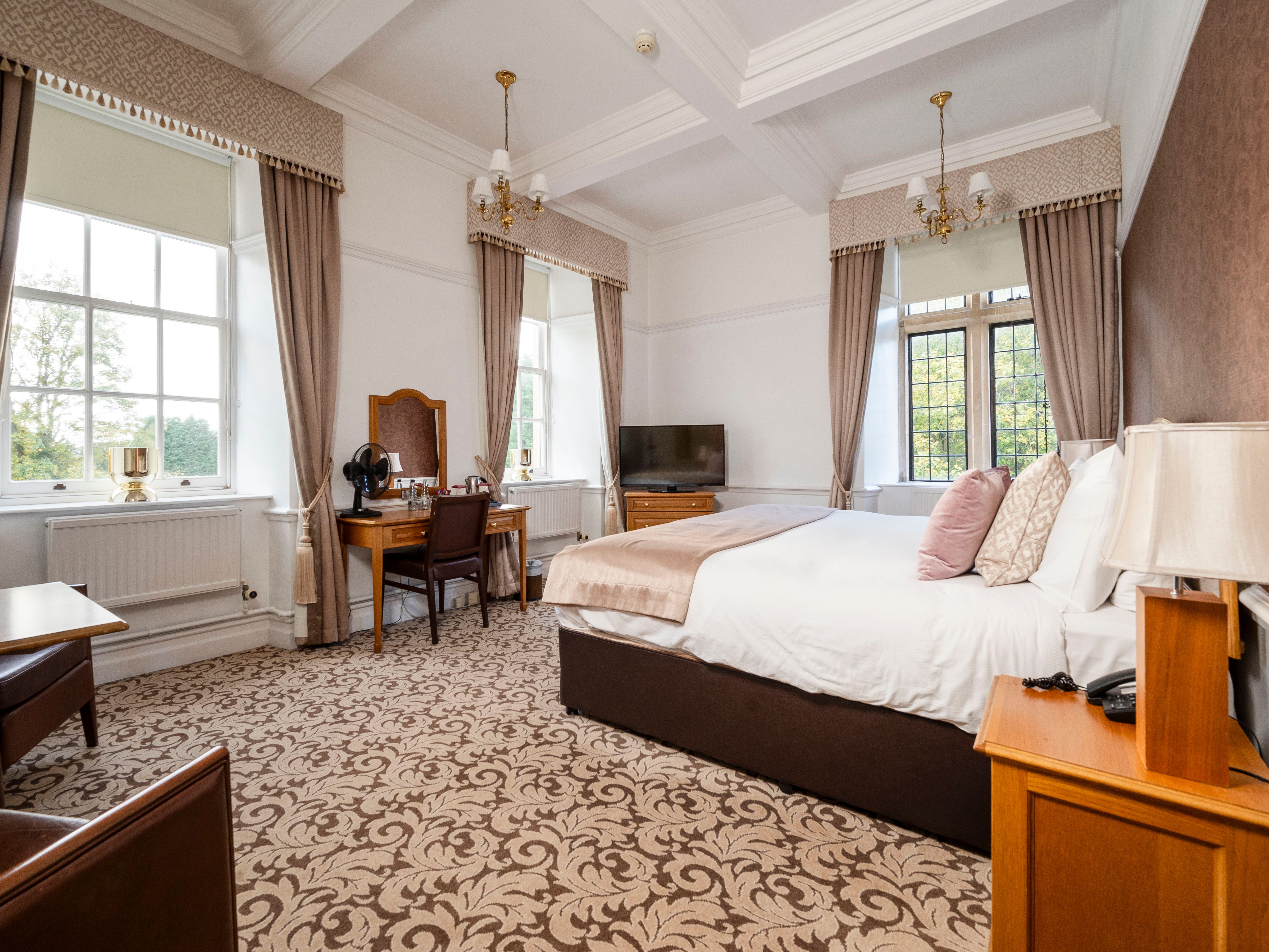 Elegant hotel room with large windows, a double bed, and classic wooden furniture.