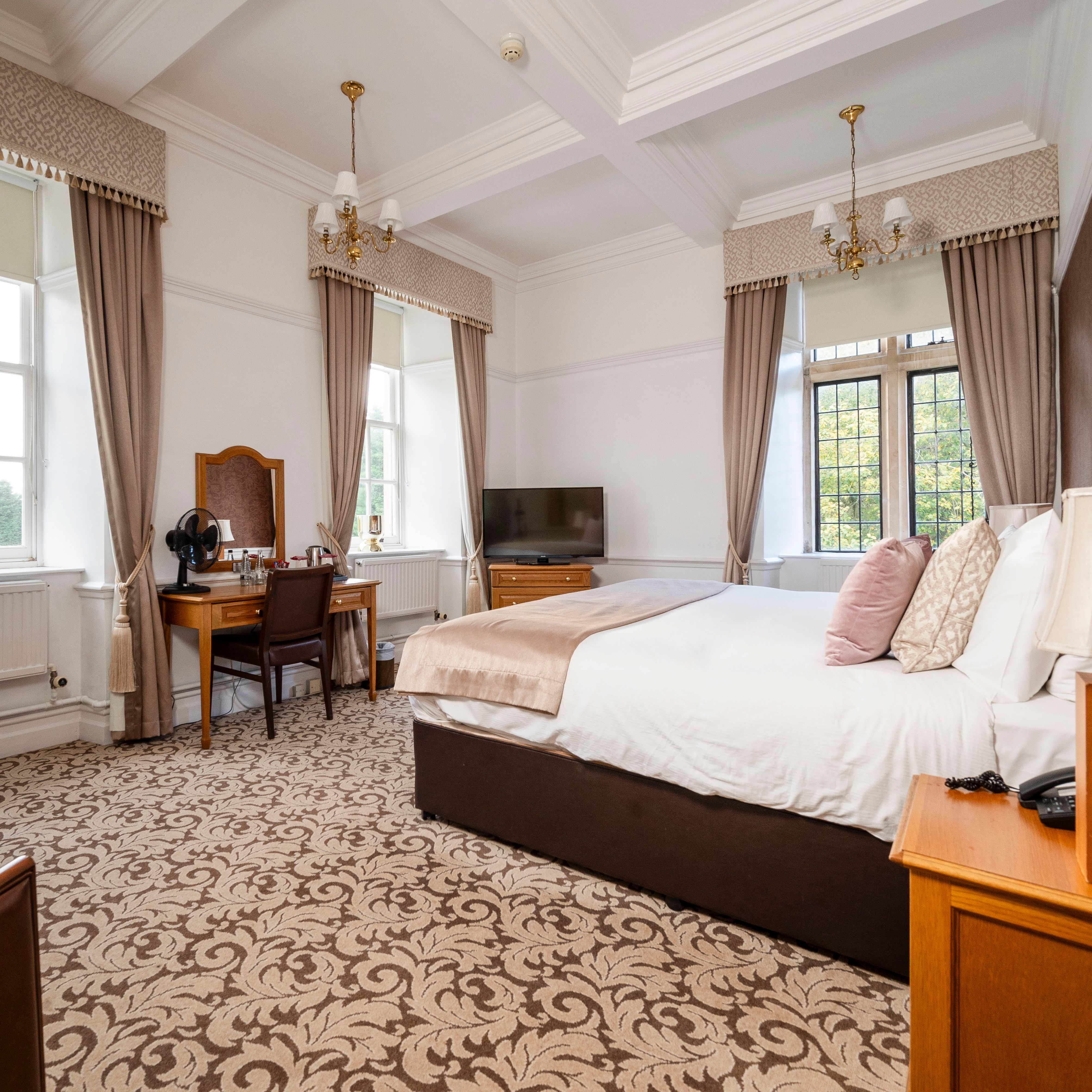 Elegant hotel room with large windows, a double bed, and classic wooden furniture.