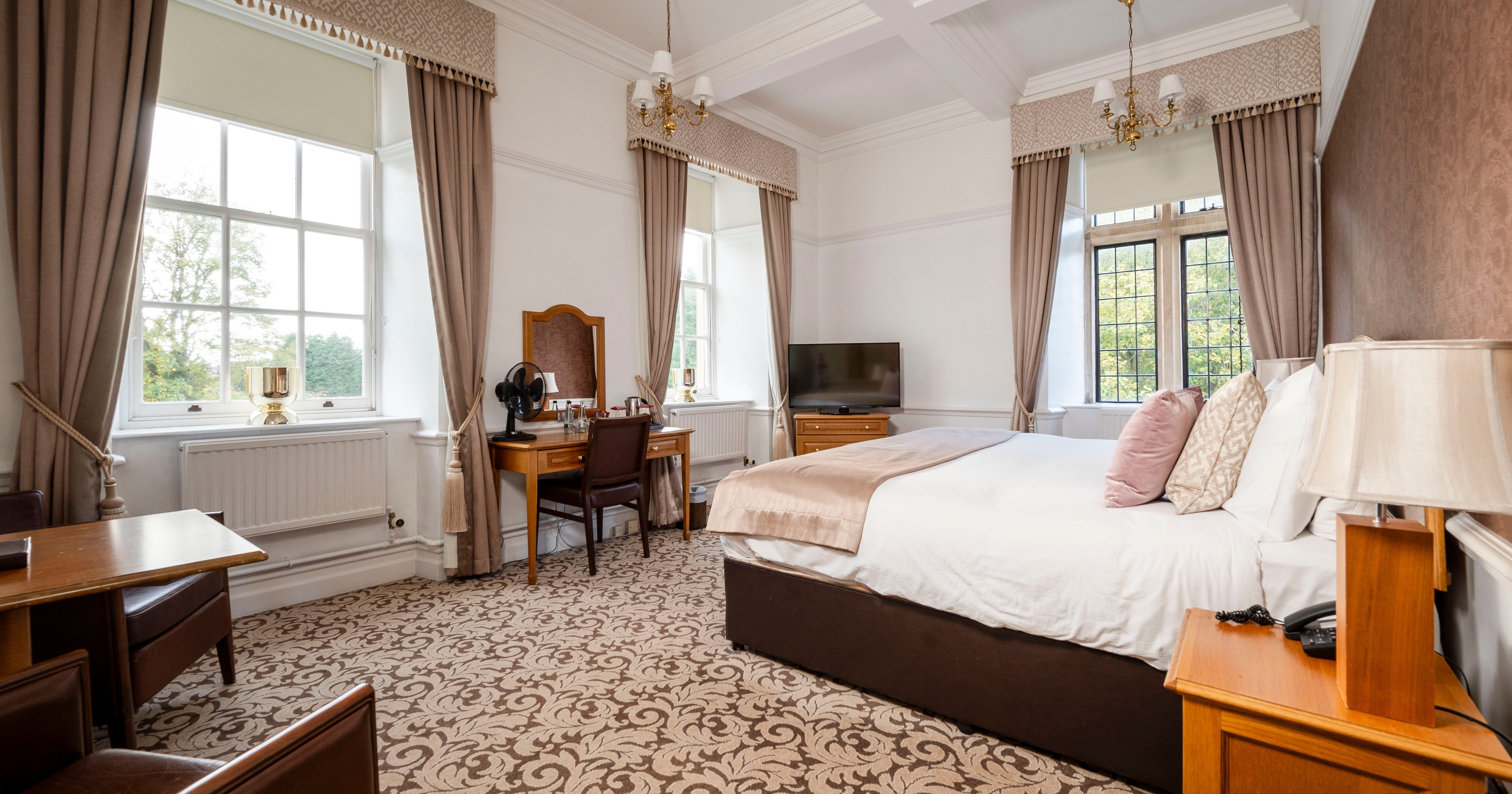 Elegant hotel room with large windows, a double bed, and classic wooden furniture.