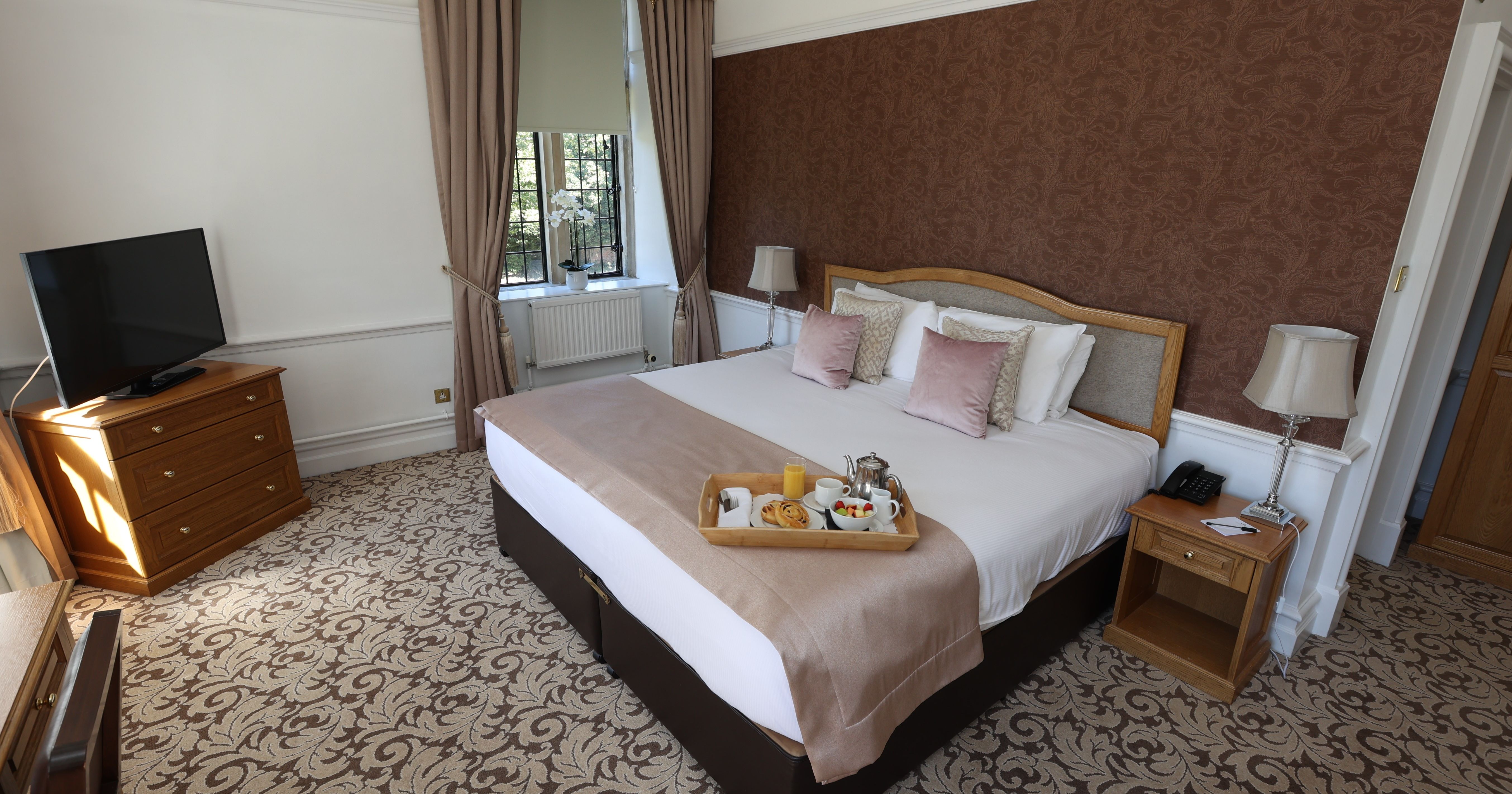 Elegant hotel room with king-size bed, breakfast tray, TV, and large window