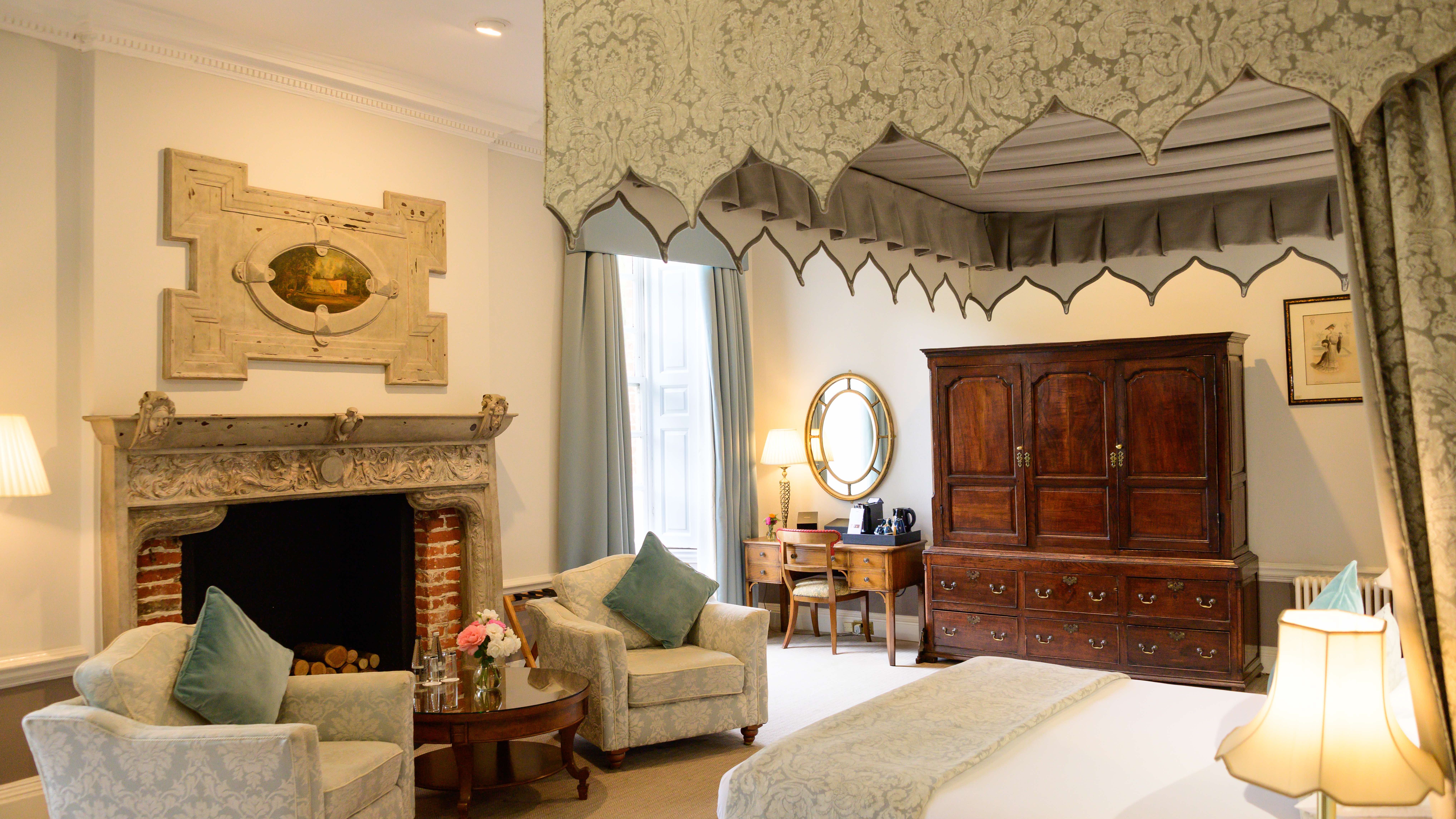 Elegant hotel room with classic furniture, canopy bed, fireplace, and sitting area.