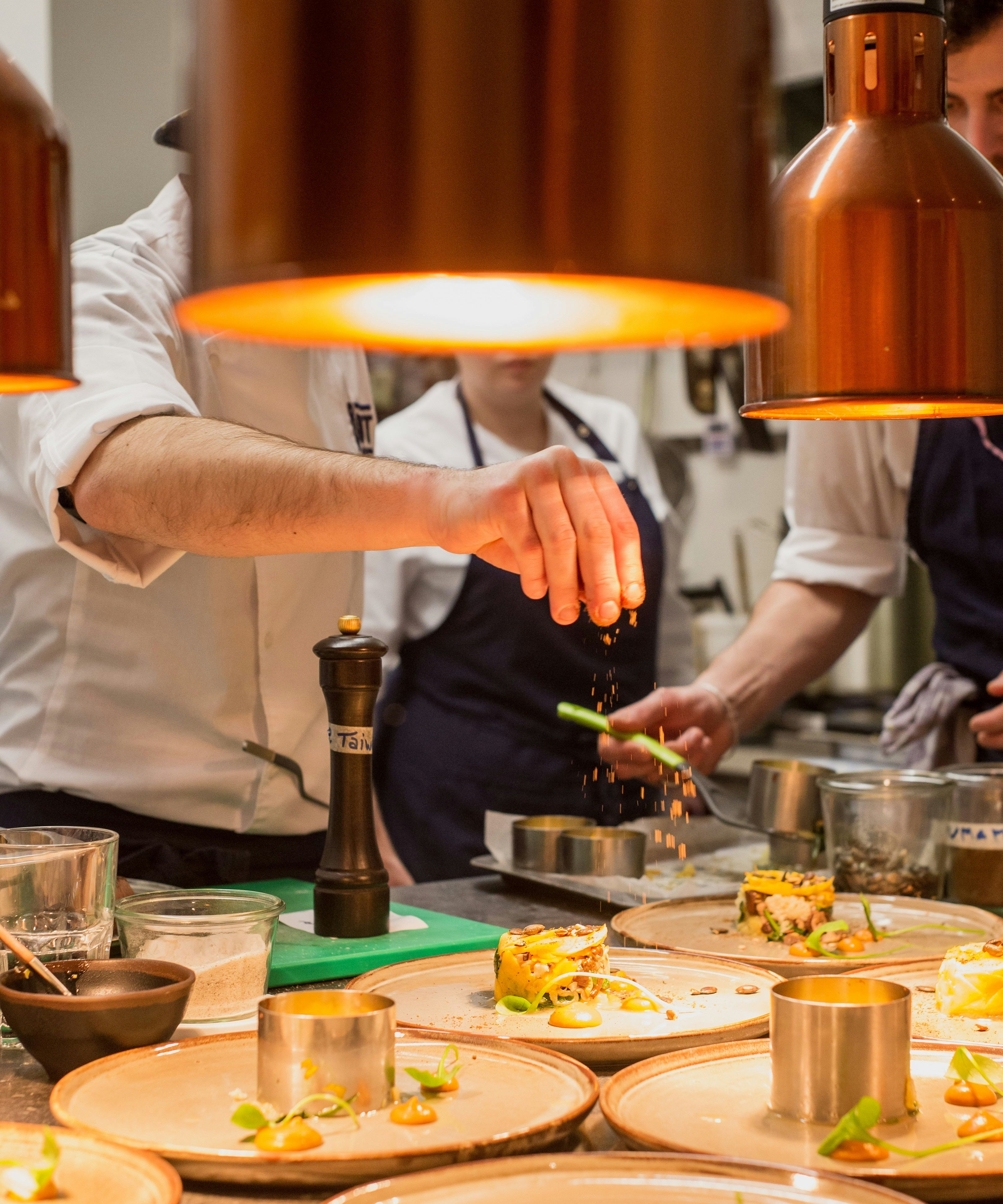 Chef garnishing plated dishes under warm kitchen lights in a professional restaurant kitchen