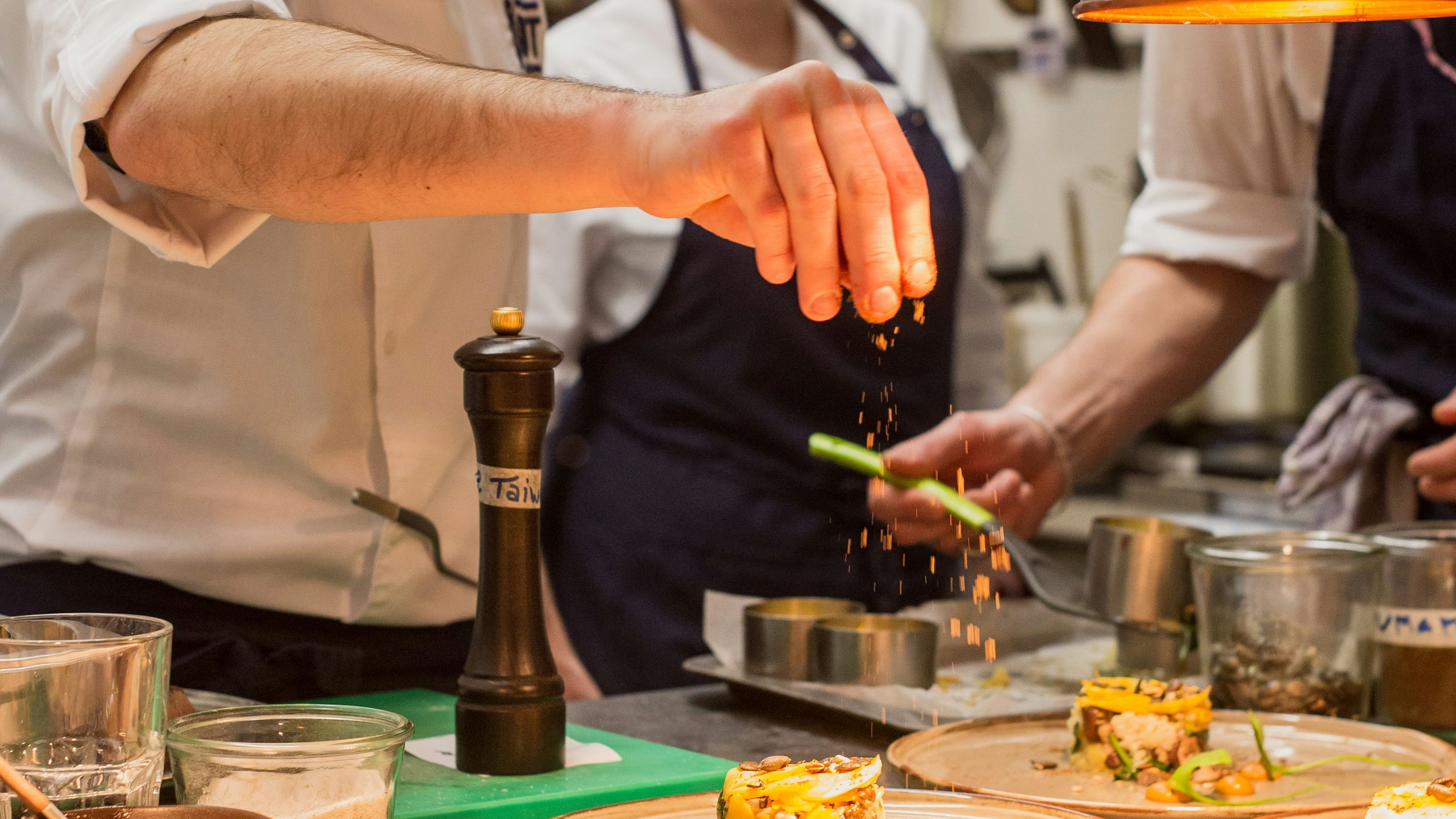 Chef garnishing plated dishes under warm kitchen lights in a professional restaurant kitchen