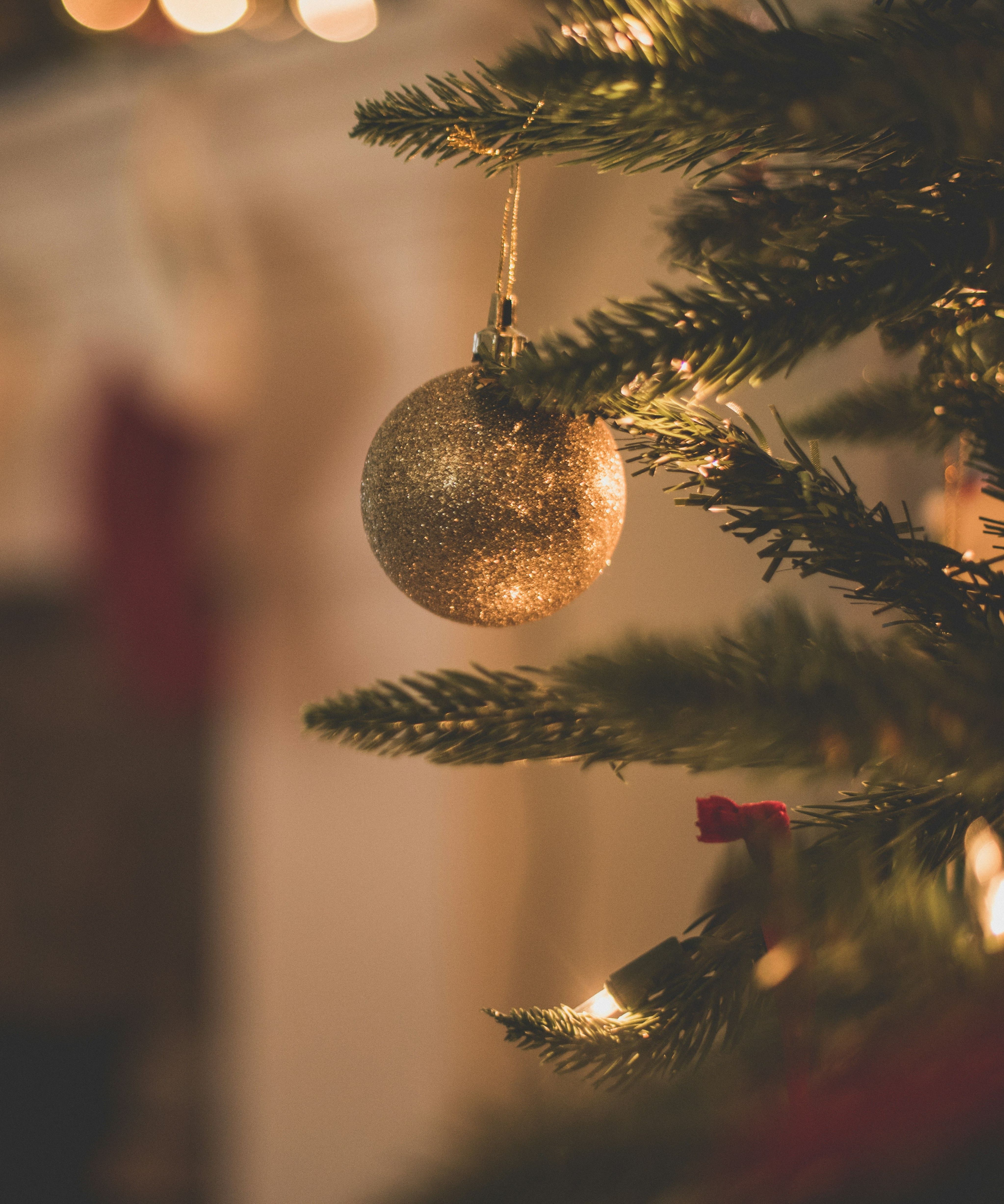 Close-up of a gold Christmas ornament hanging on a decorated tree with stockings and festive lights in the background.