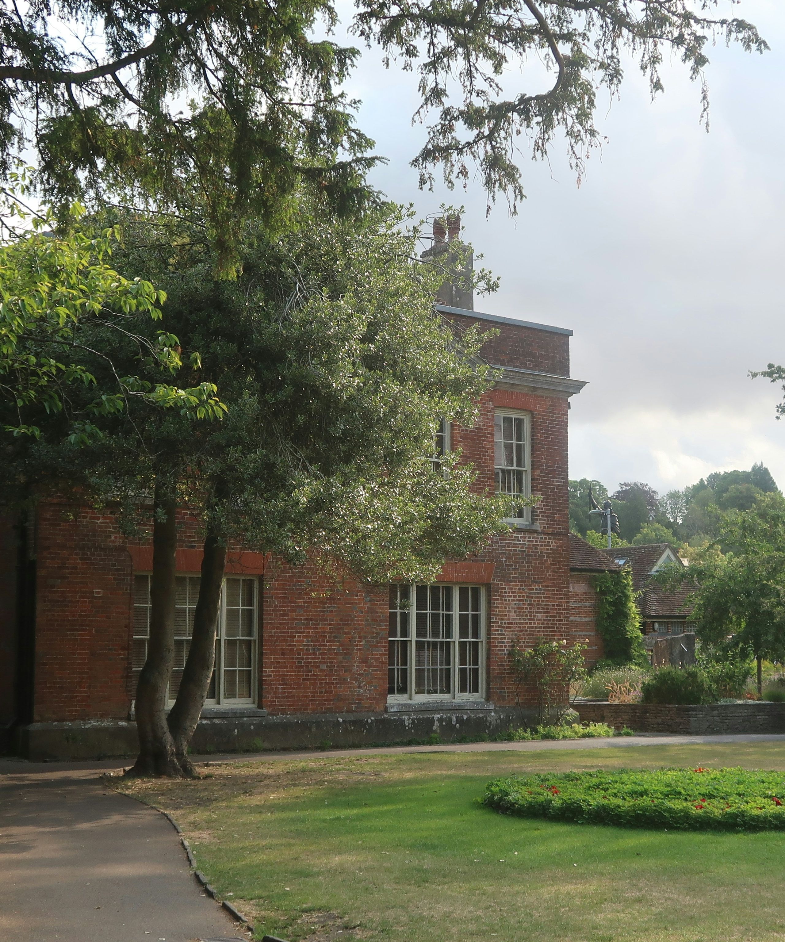 Red brick building surrounded by trees and a garden with a walking path