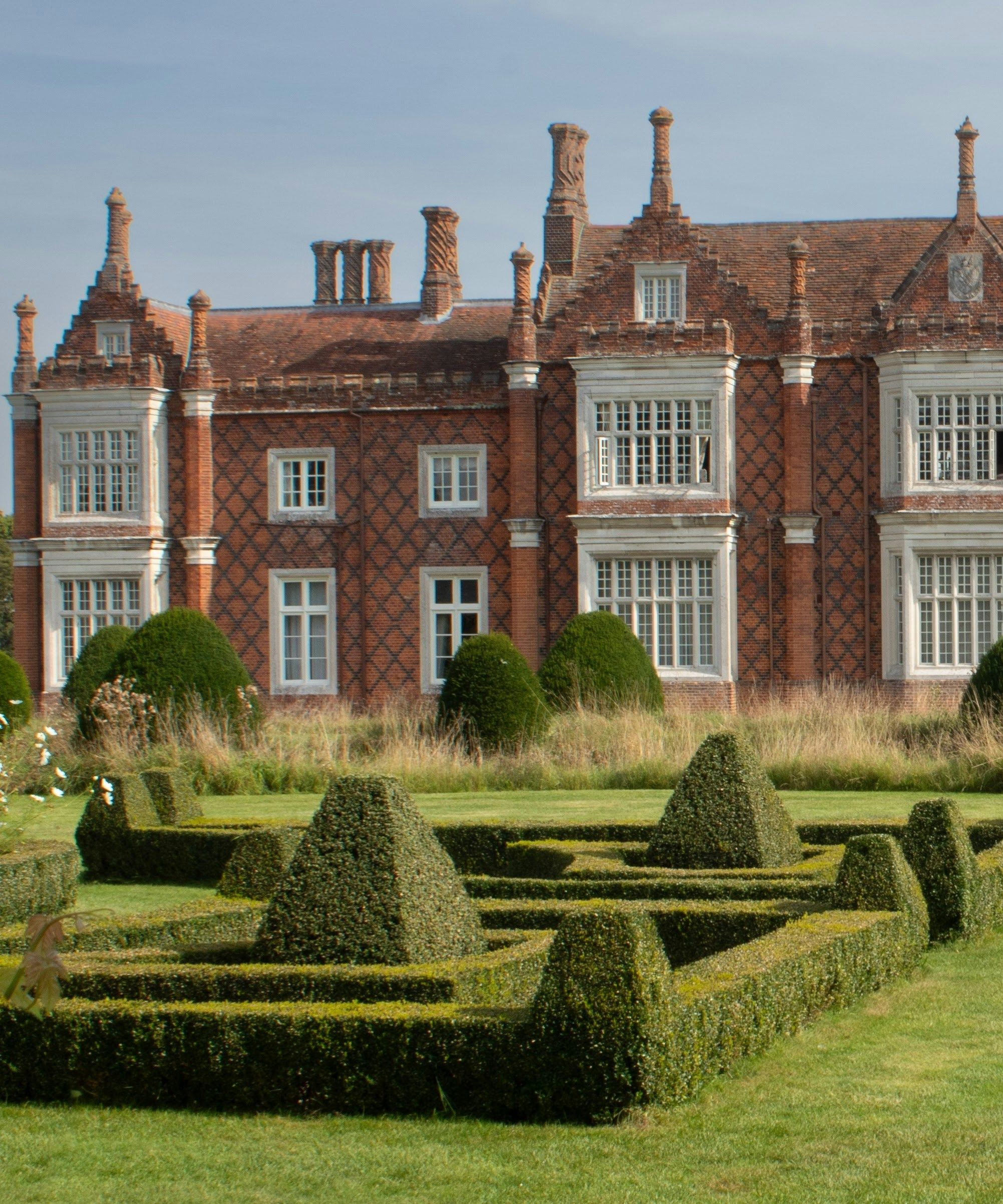 Historic English manor house with elaborate brickwork and formal garden hedges