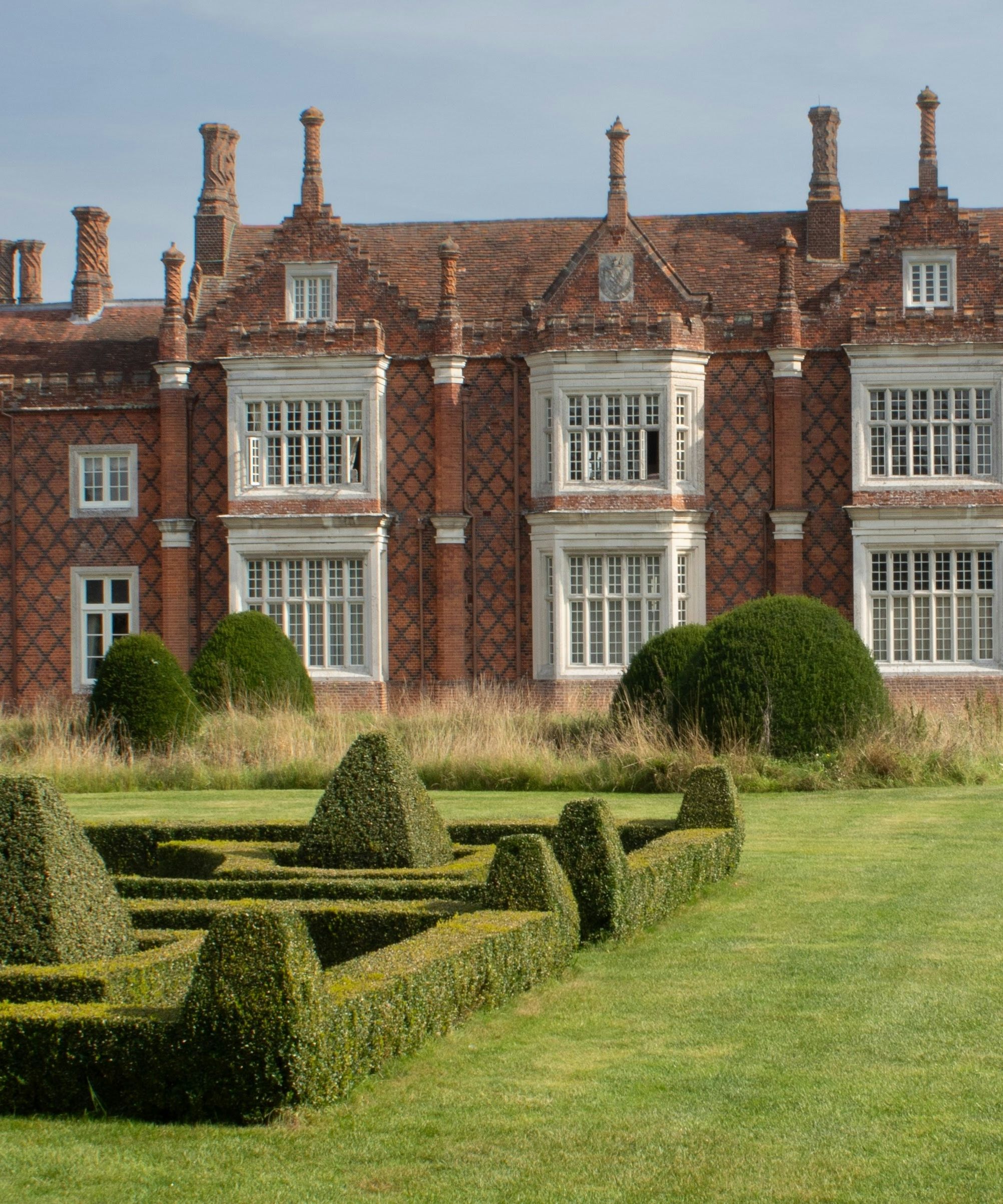 Historic English manor house with elaborate brickwork and formal garden hedges