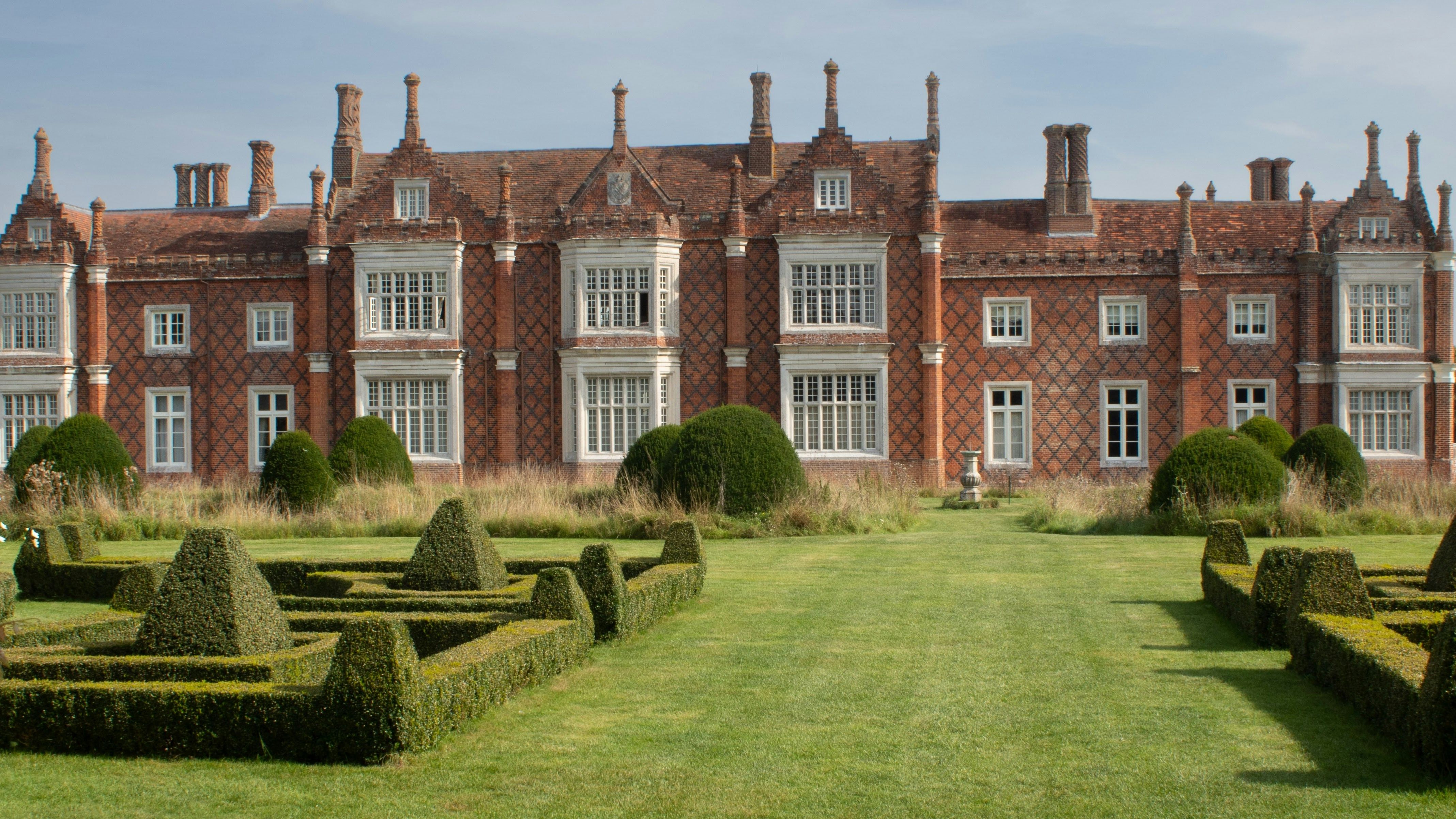 Historic English manor house with elaborate brickwork and formal garden hedges