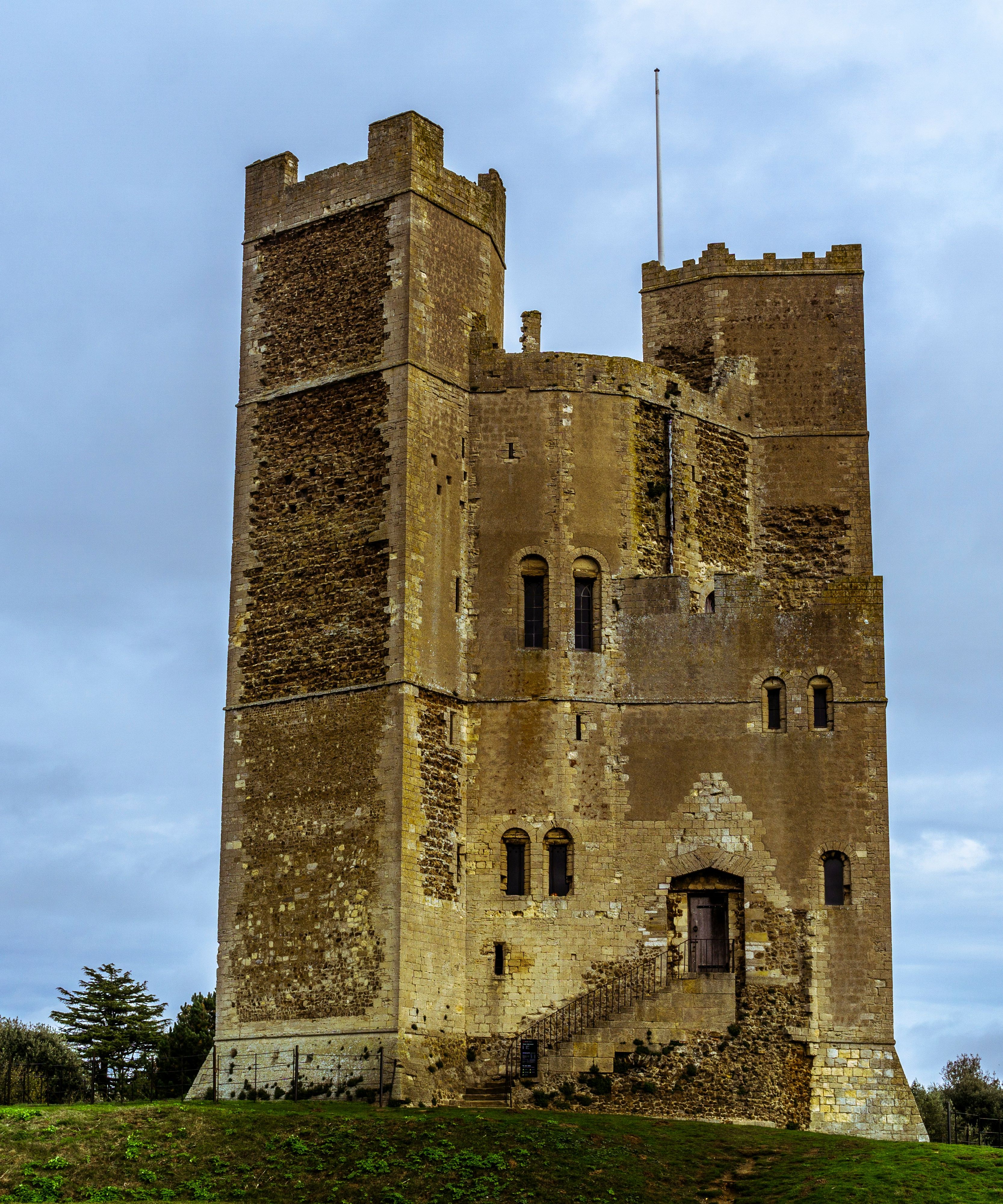 Medieval stone castle with battlements on a grassy hill under a cloudy sky