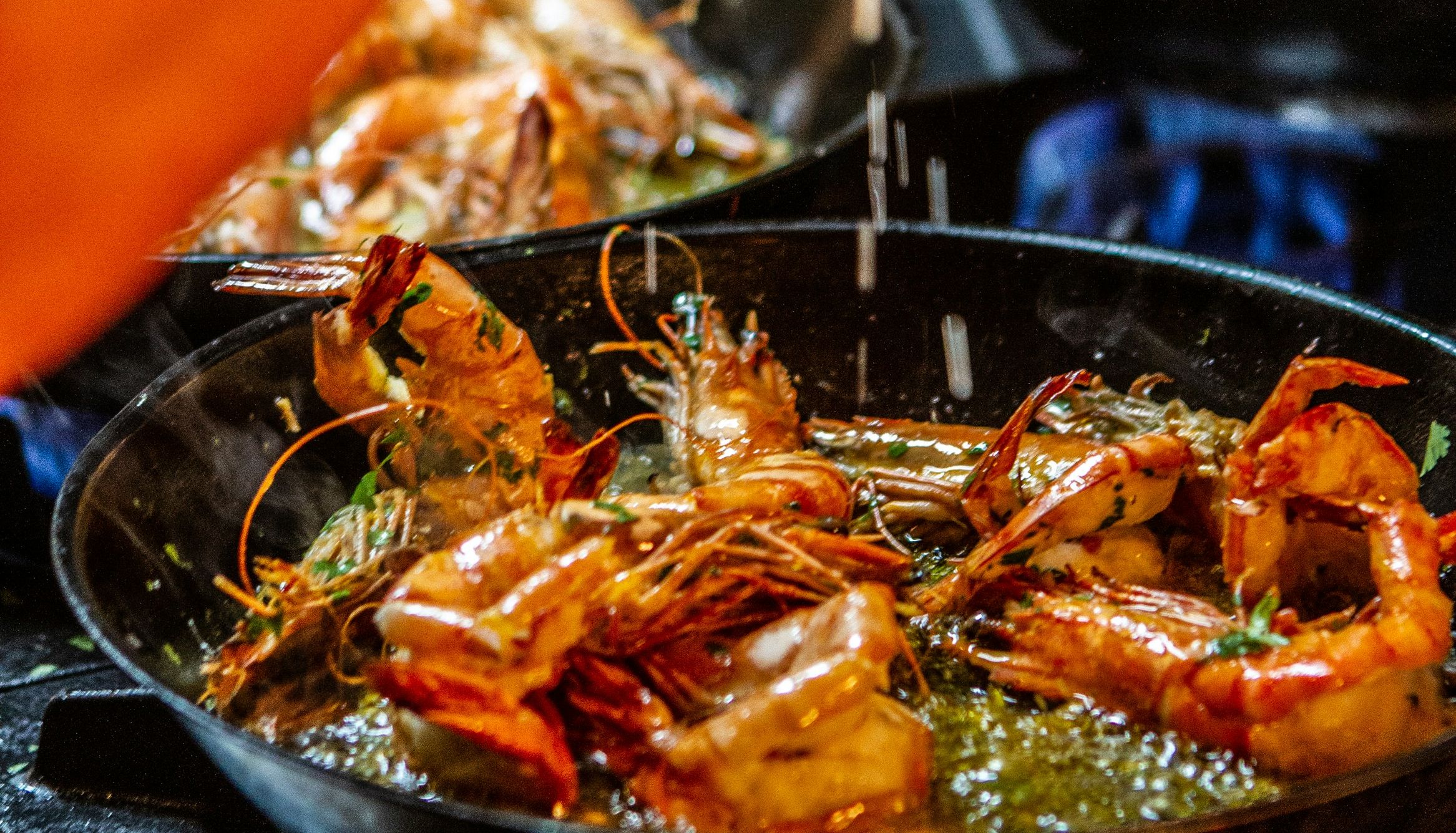 A person seasoning shrimp while cooking them in a pan on a stove.