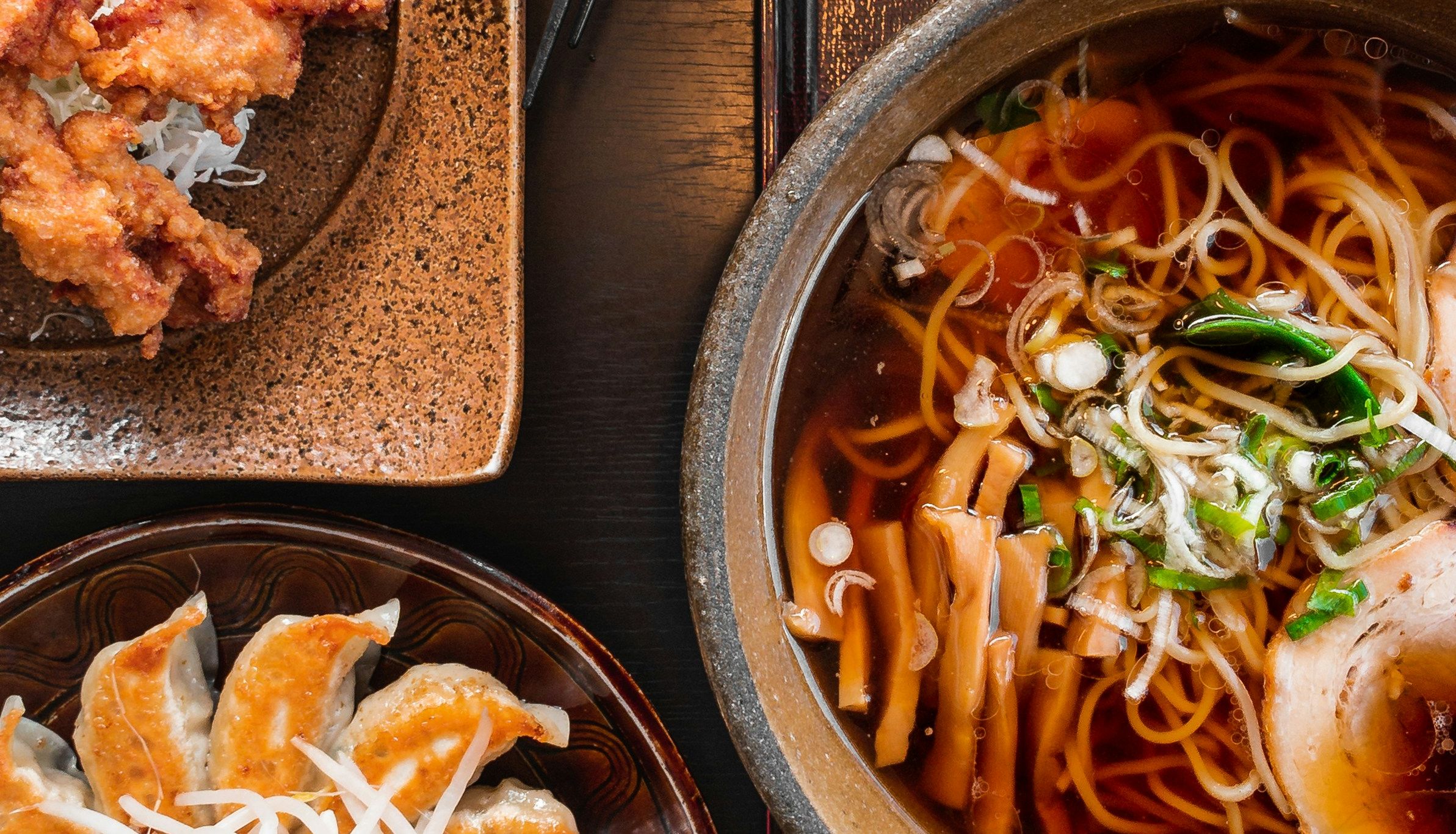 Top view of Japanese food including ramen, gyoza, and fried chicken on a table.