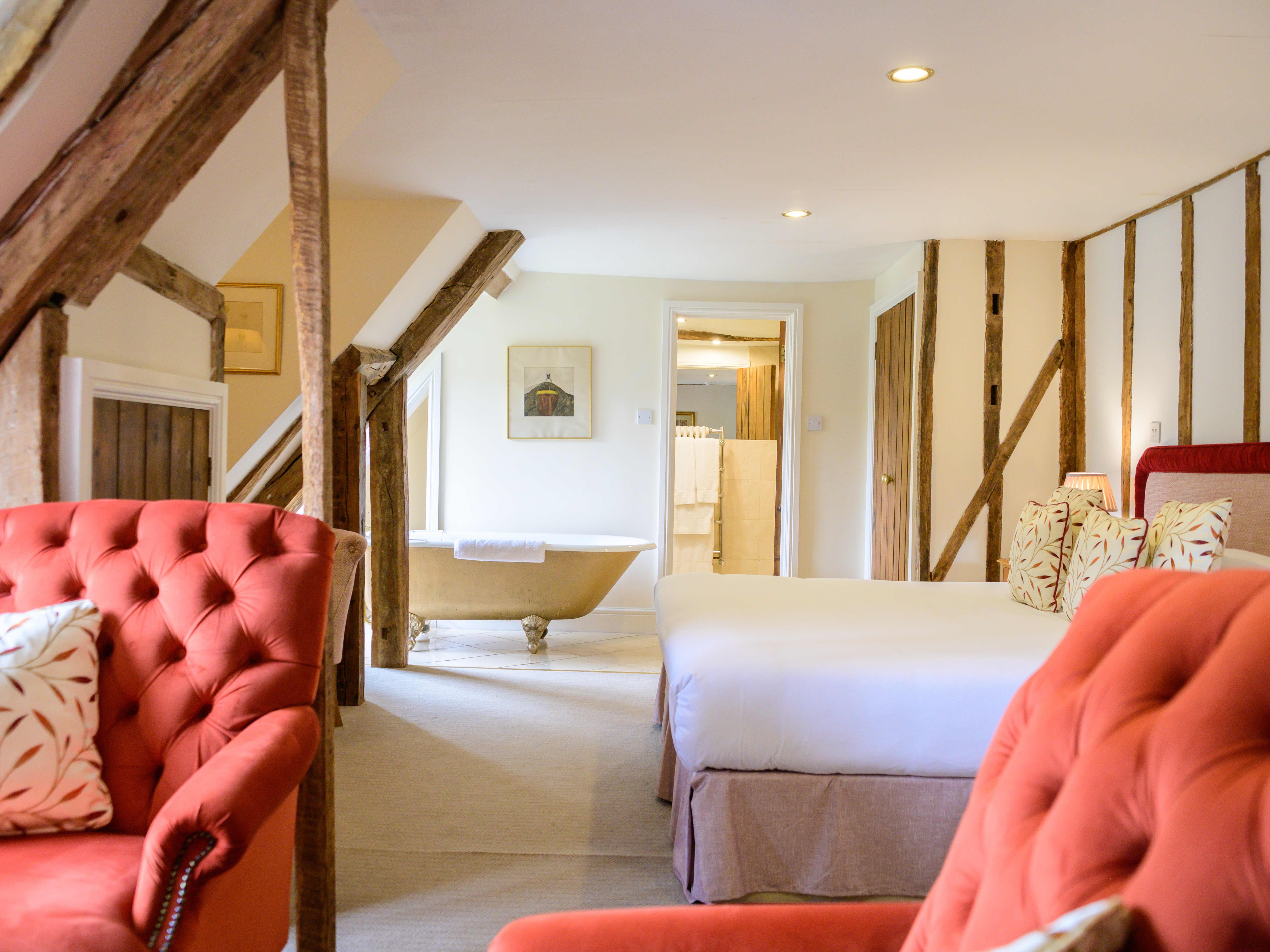 Cozy rustic bedroom with exposed wooden beams, red armchairs, and a freestanding bathtub