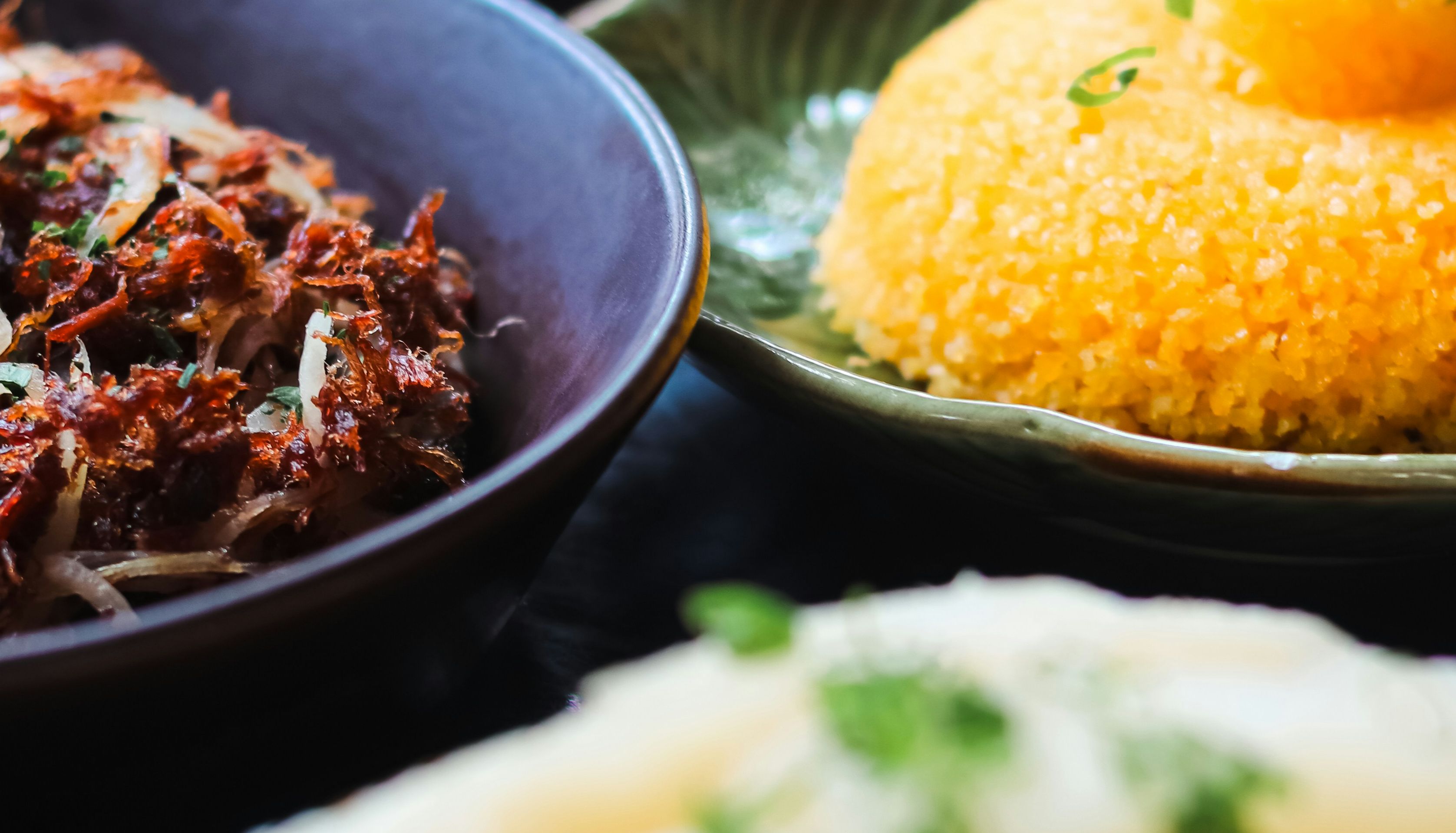 Three plates of assorted food dishes including shredded meat, yellow rice, and cassava.