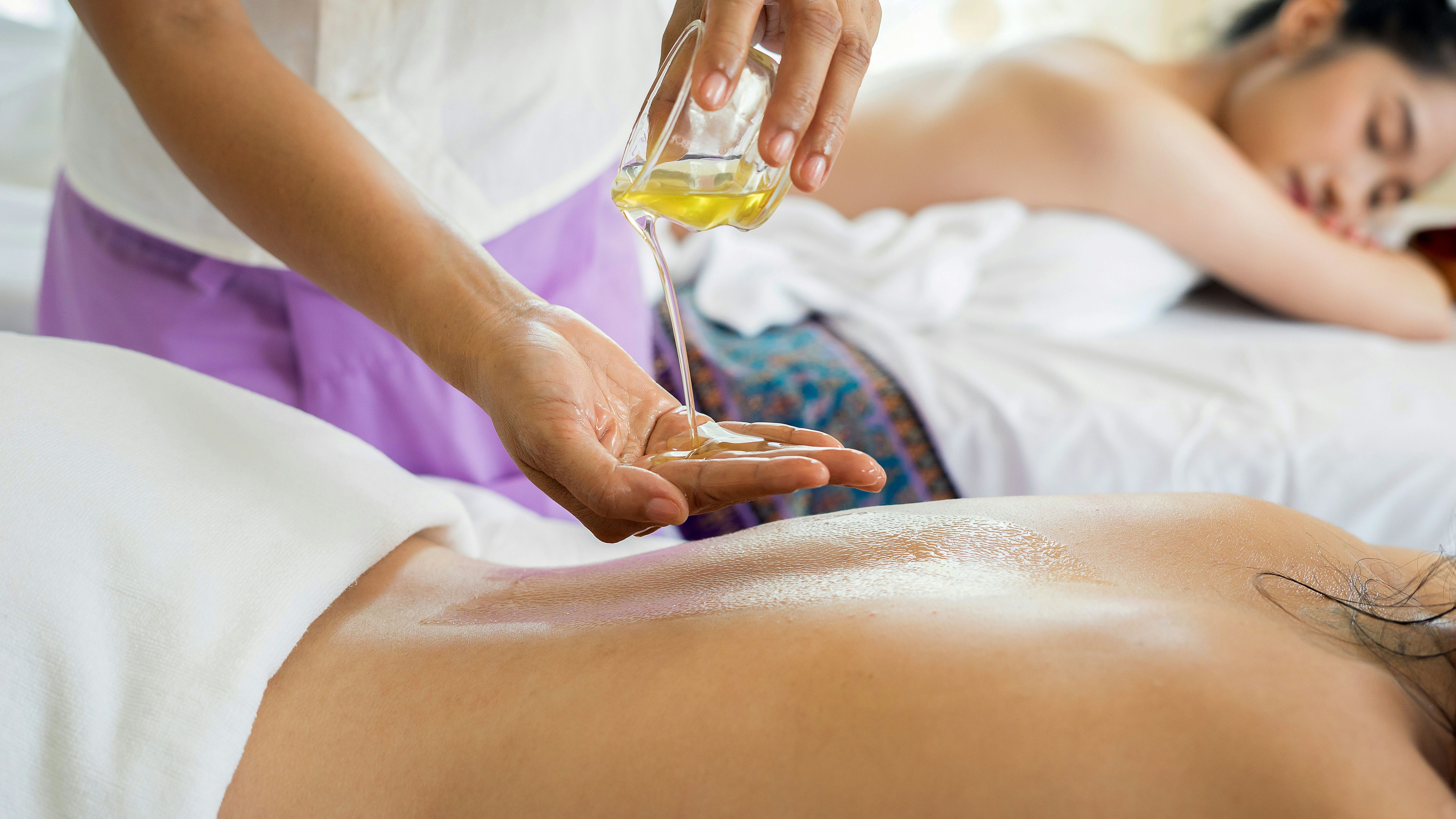 Massage therapist pouring oil onto a client's back during a spa treatment