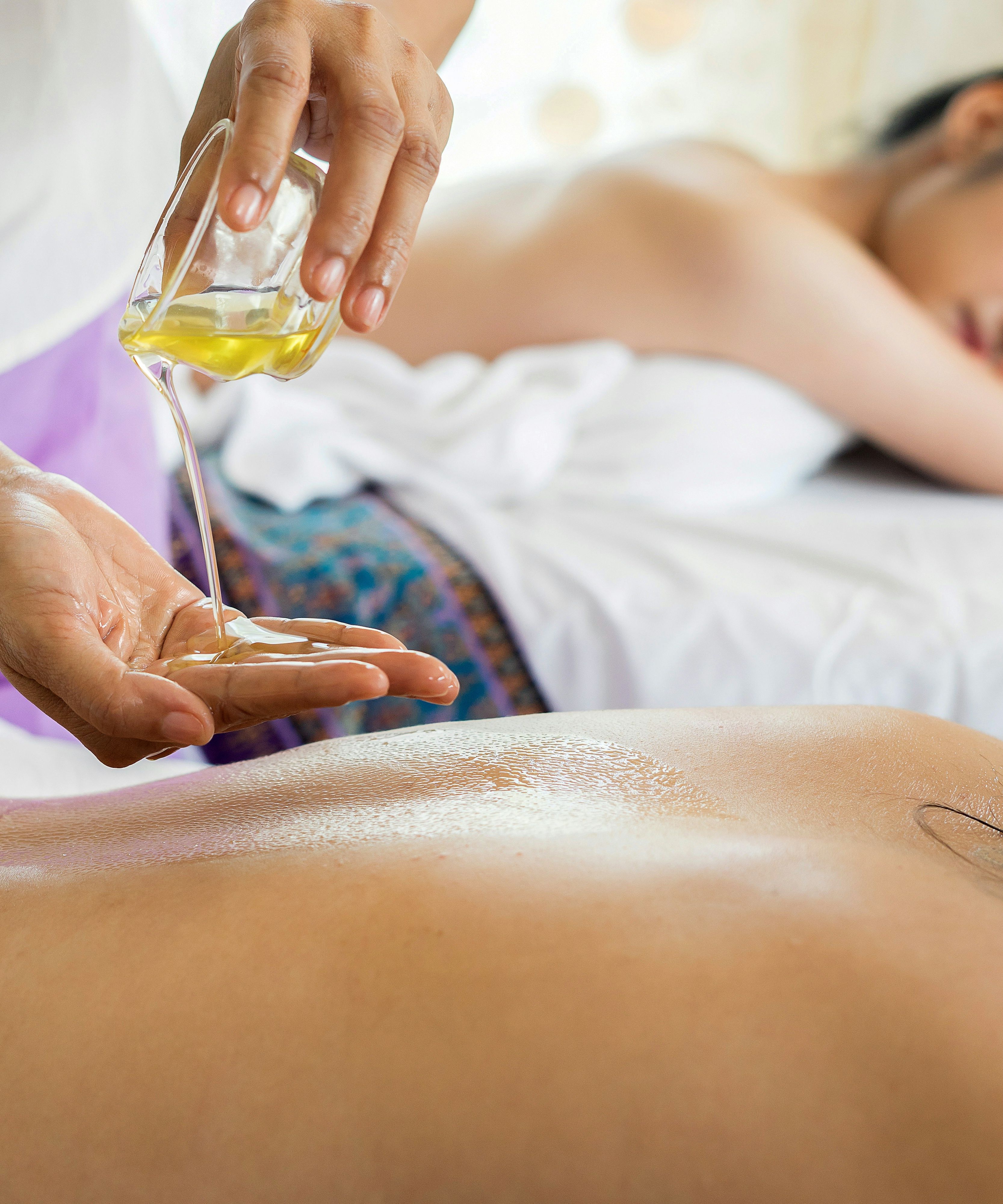 Massage therapist pouring oil onto a client's back during a spa treatment