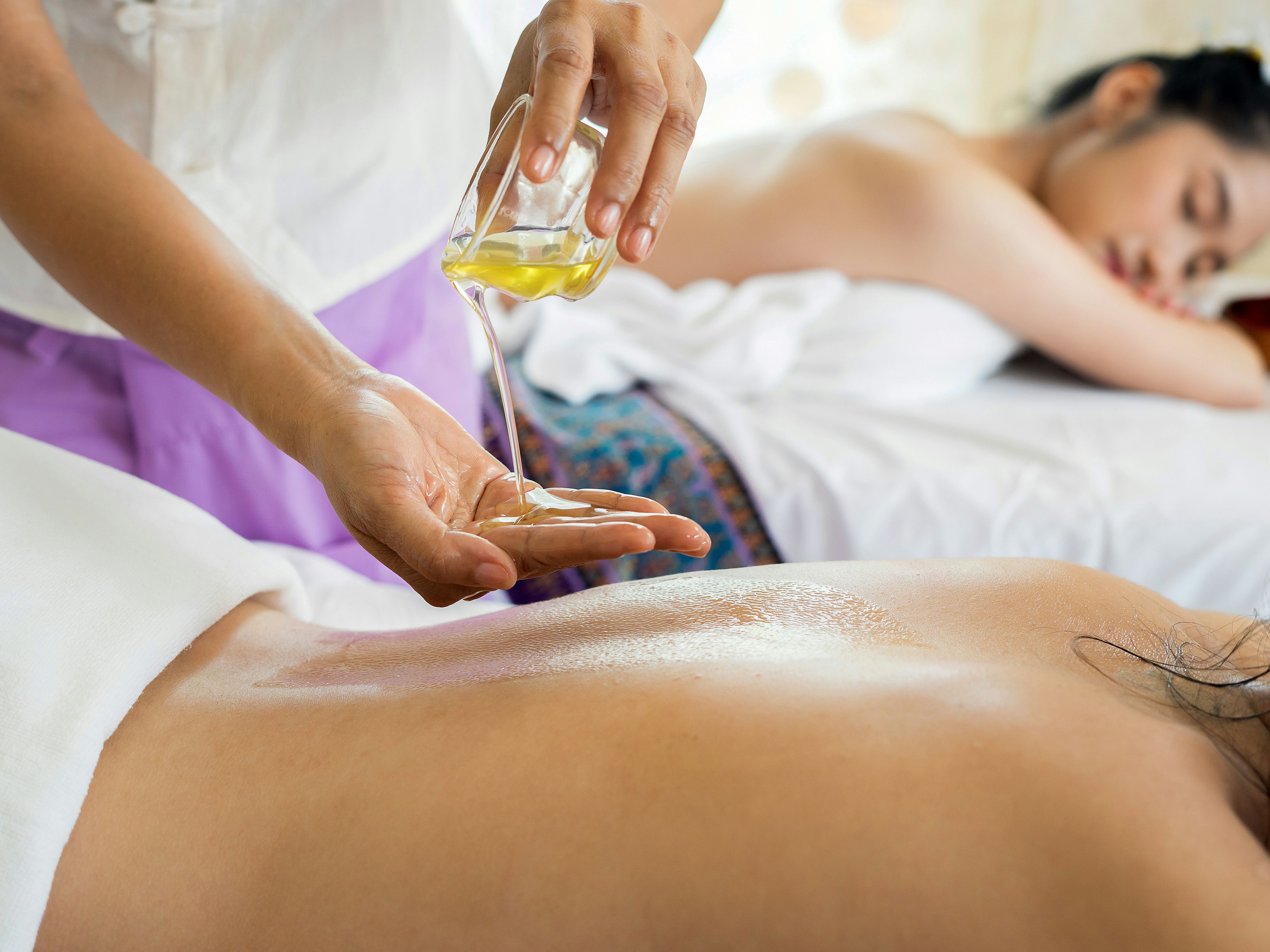 Massage therapist pouring oil onto a client's back during a spa treatment
