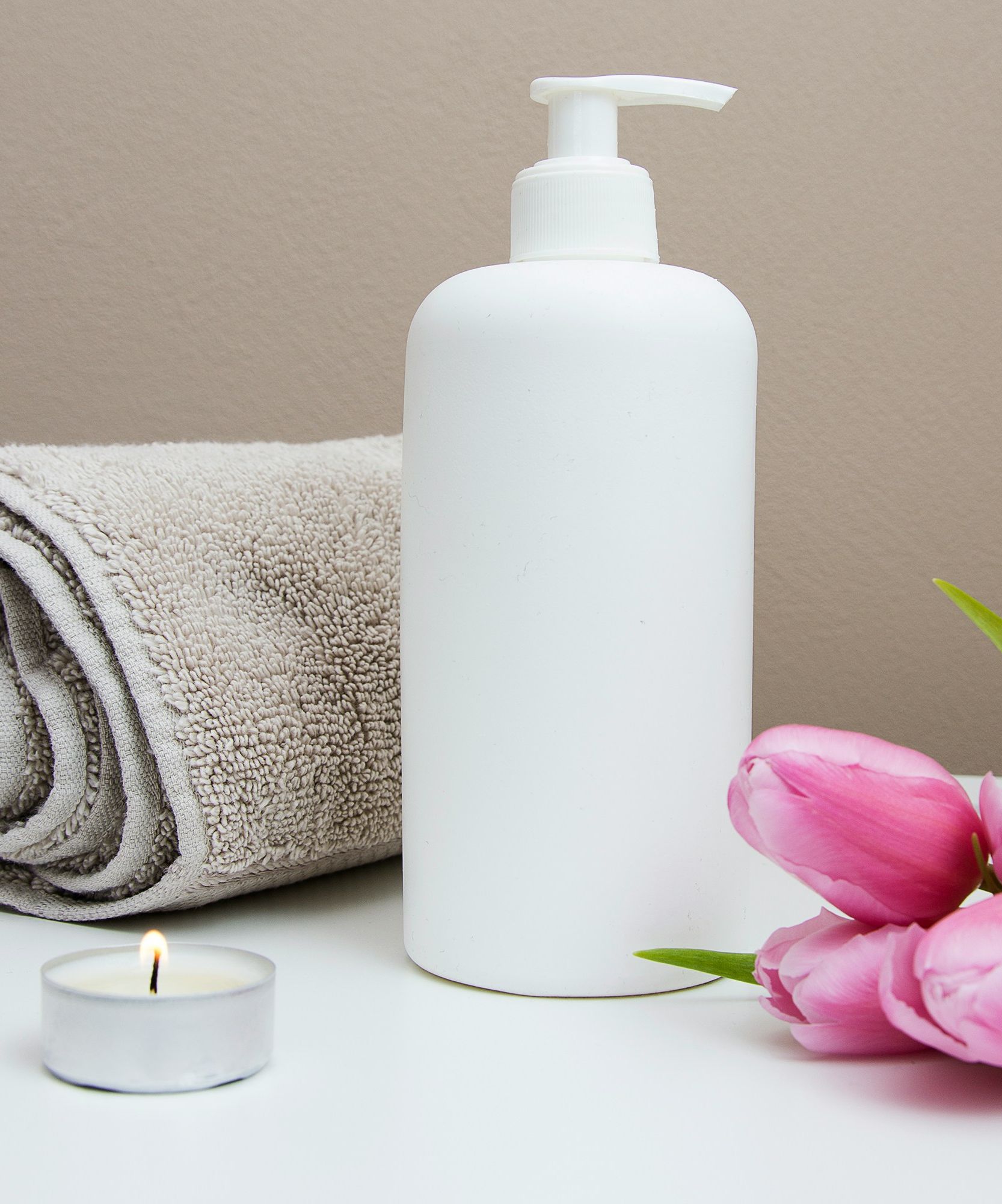 Spa setting with a rolled towel, lotion bottle, pink tulips, and a lit tealight candle