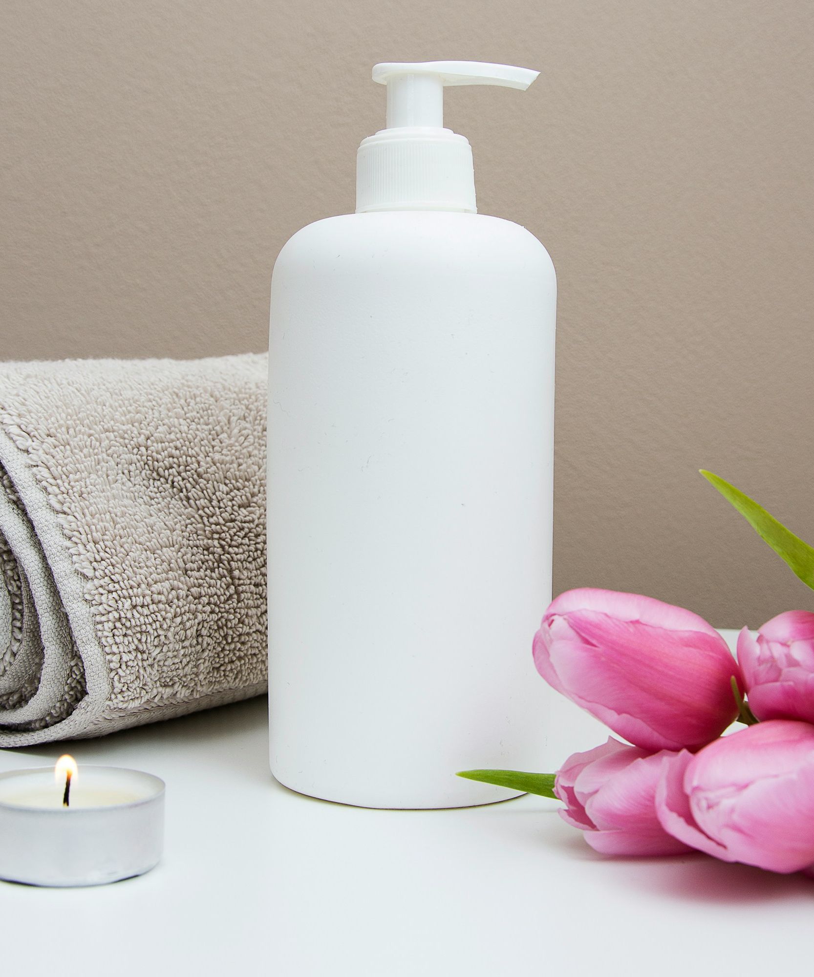 Spa setting with a rolled towel, lotion bottle, pink tulips, and a lit tealight candle