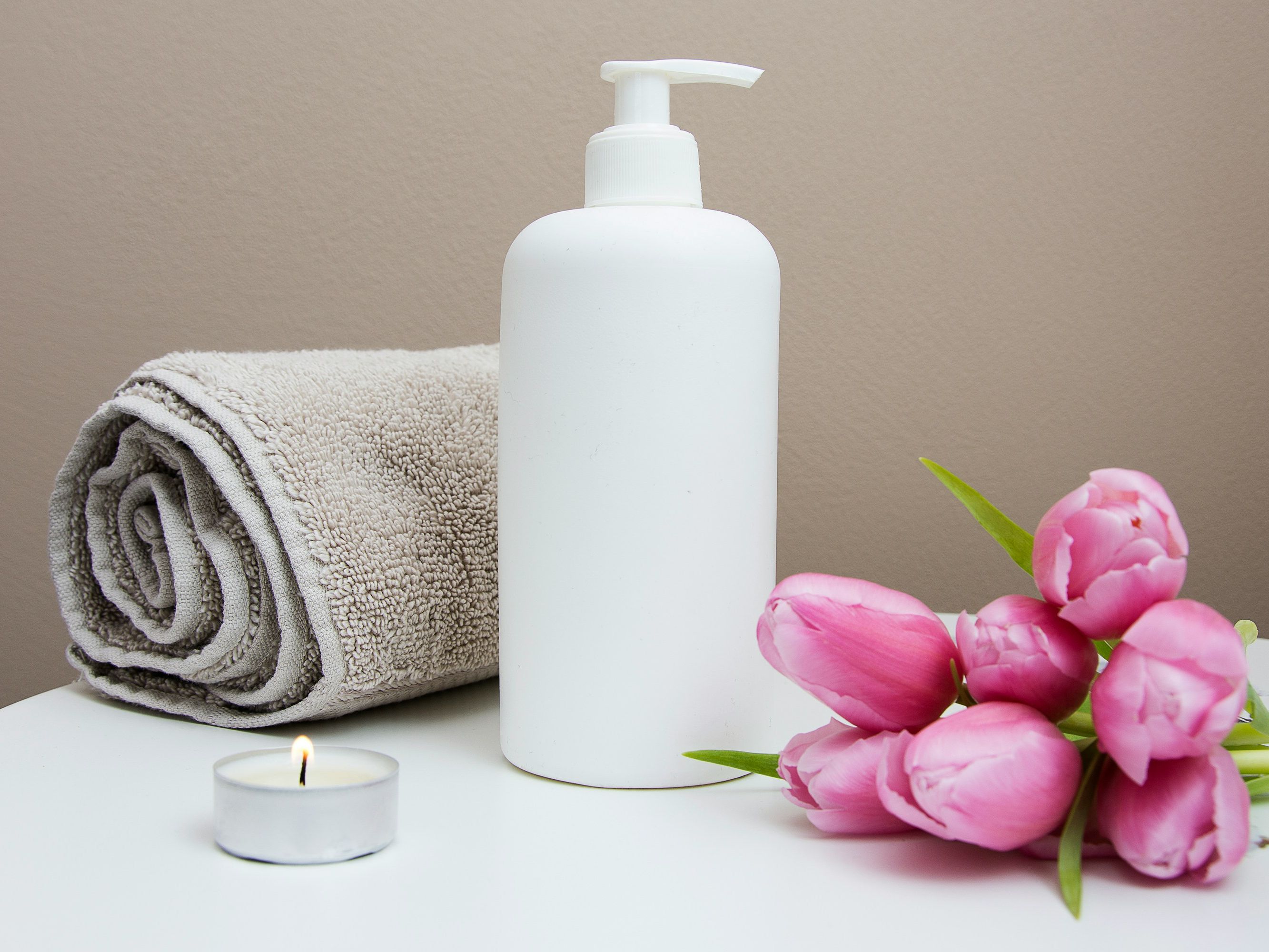 Spa setting with a rolled towel, lotion bottle, pink tulips, and a lit tealight candle