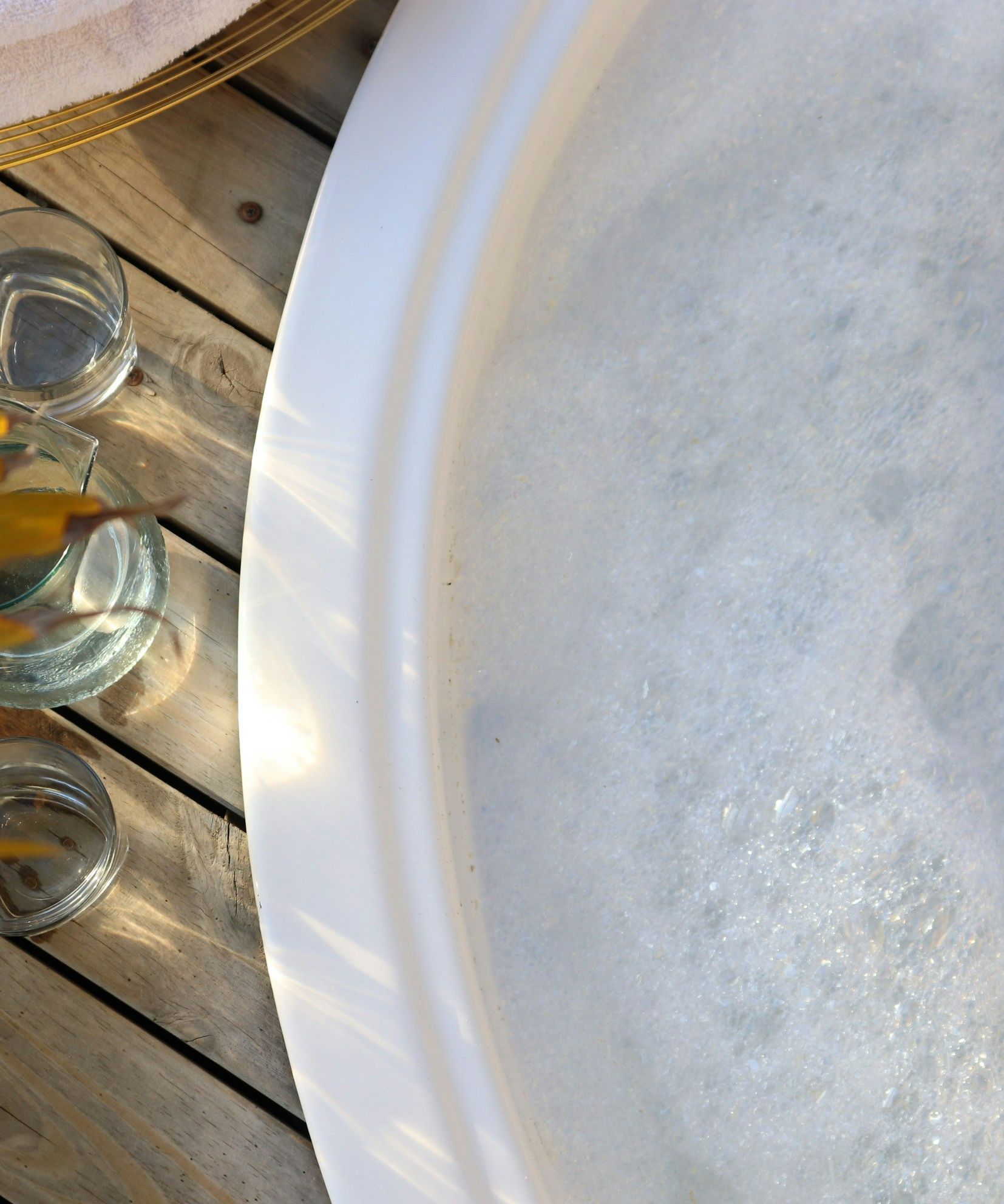 Close-up of a bubbling jacuzzi next to wooden deck with water glasses, a plant, and a folded towel.