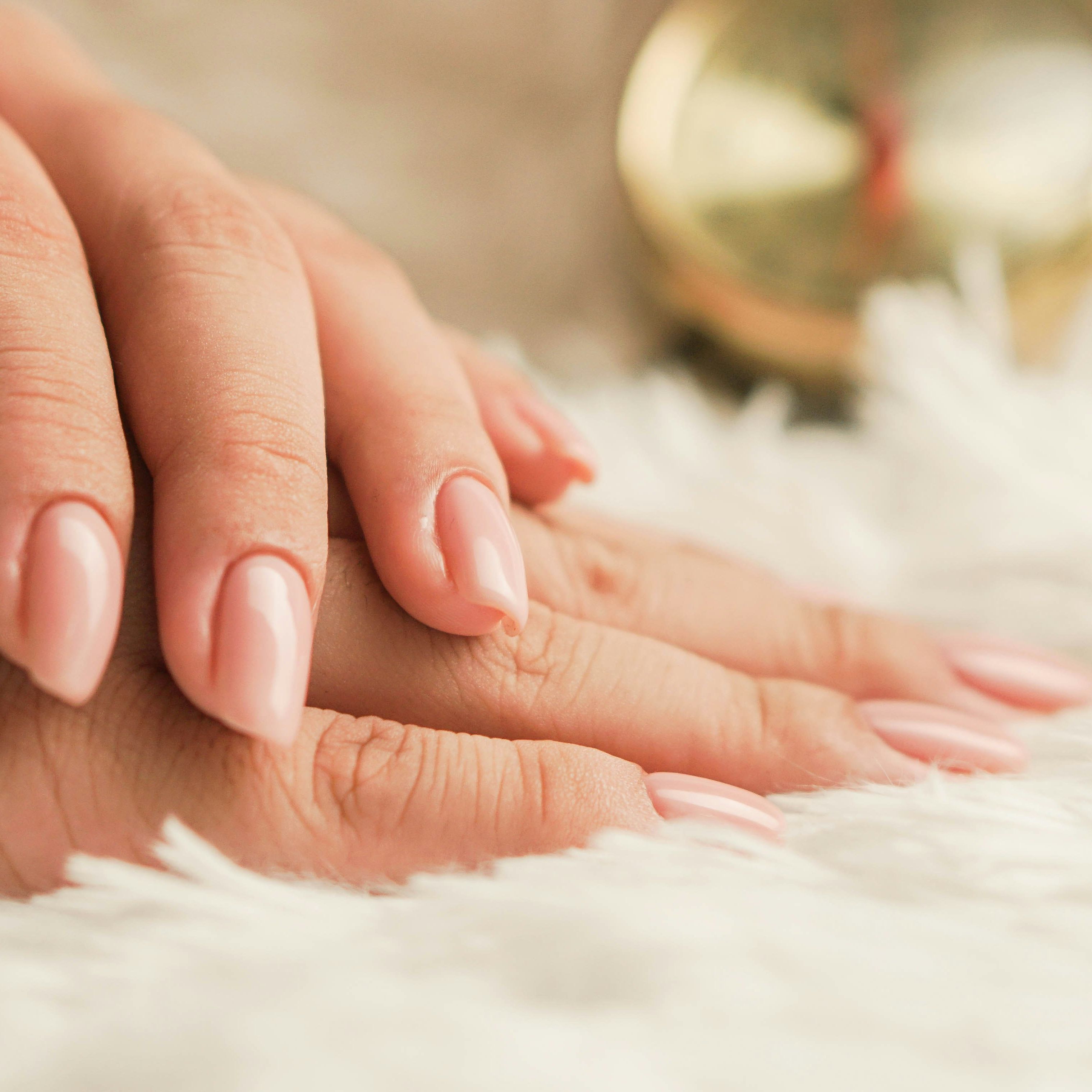 Close-up of hands with nude-colored manicured nails resting on a soft white surface