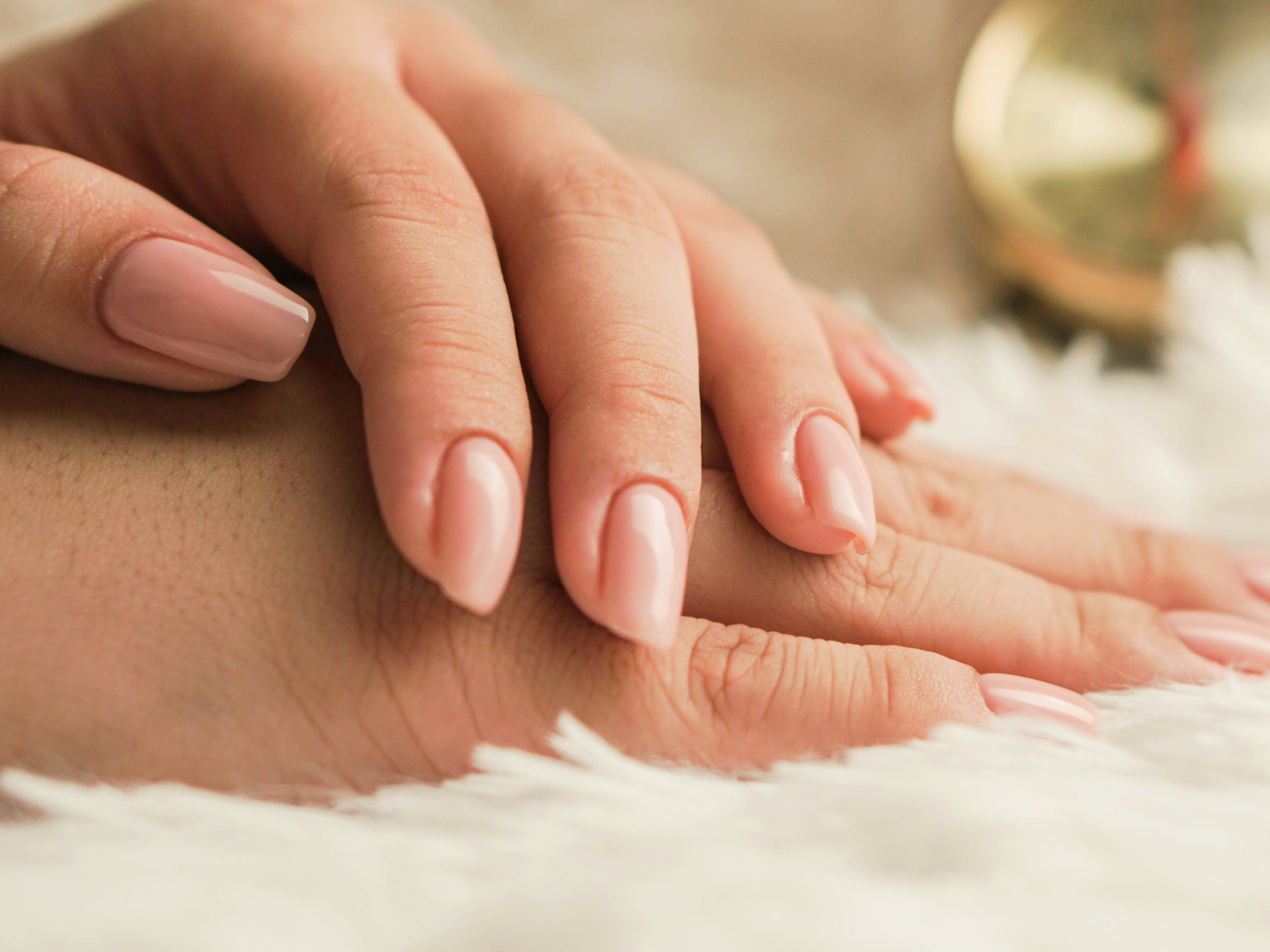 Close-up of hands with nude-colored manicured nails resting on a soft white surface