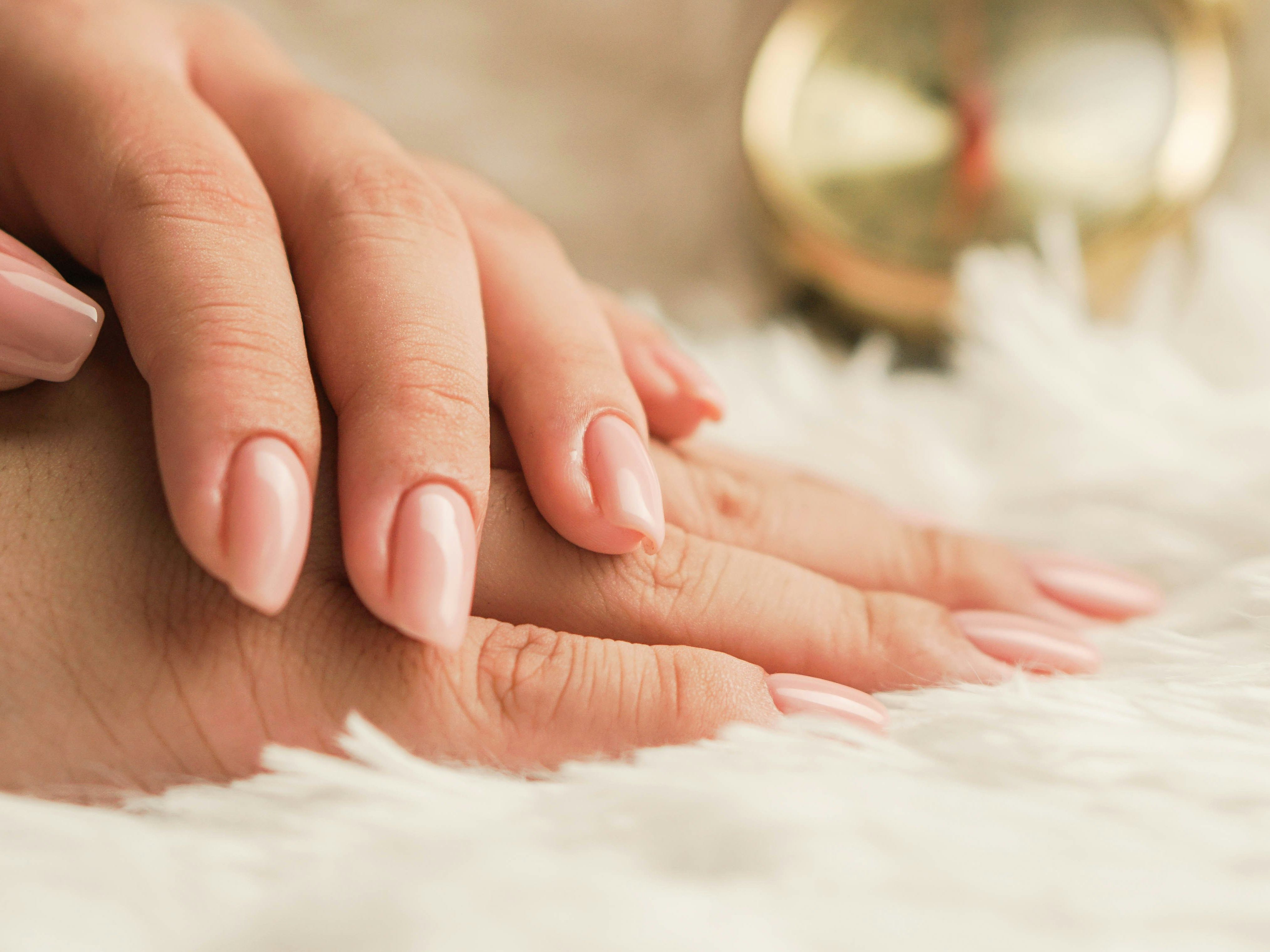 Close-up of hands with nude-colored manicured nails resting on a soft white surface