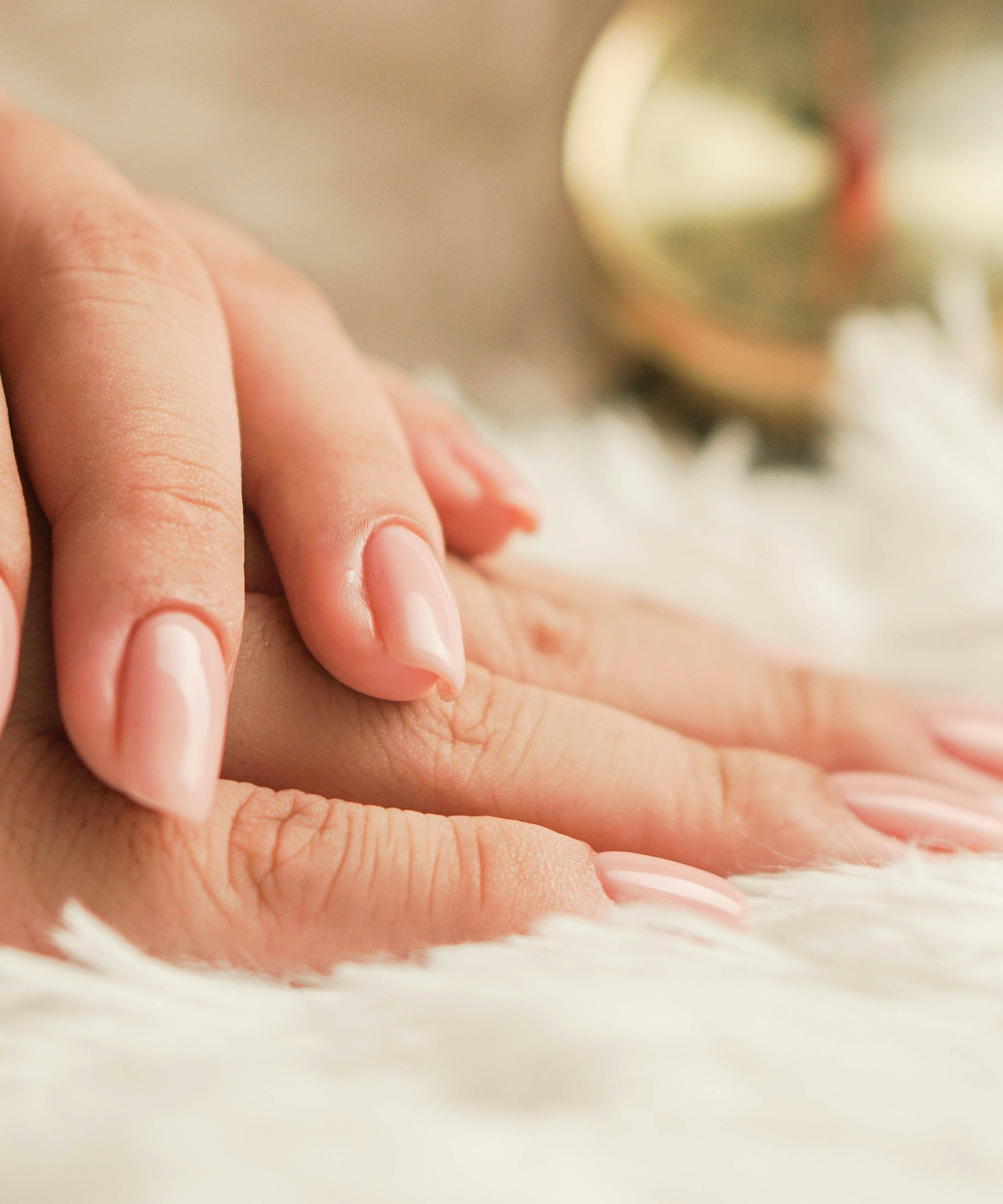 Close-up of hands with nude-colored manicured nails resting on a soft white surface