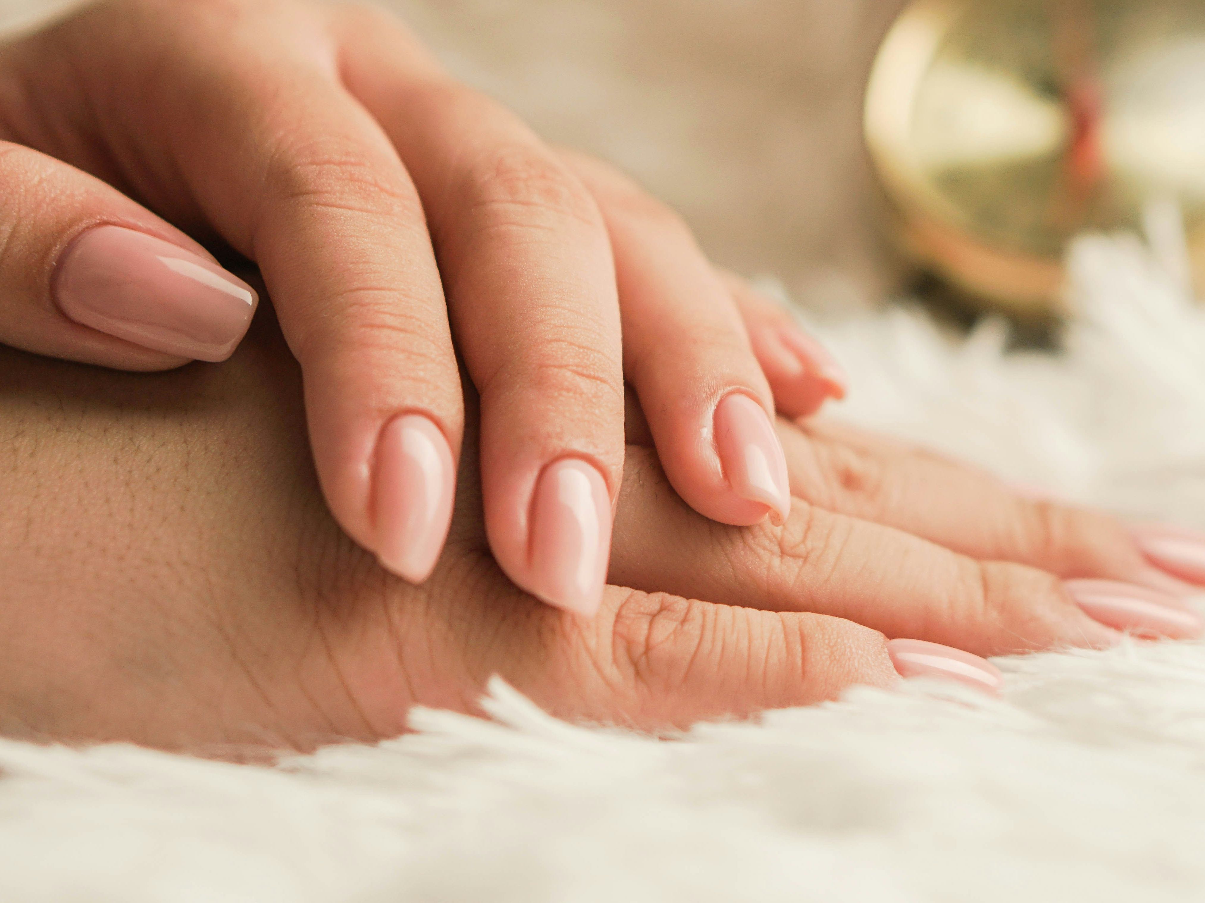 Close-up of hands with nude-colored manicured nails resting on a soft white surface