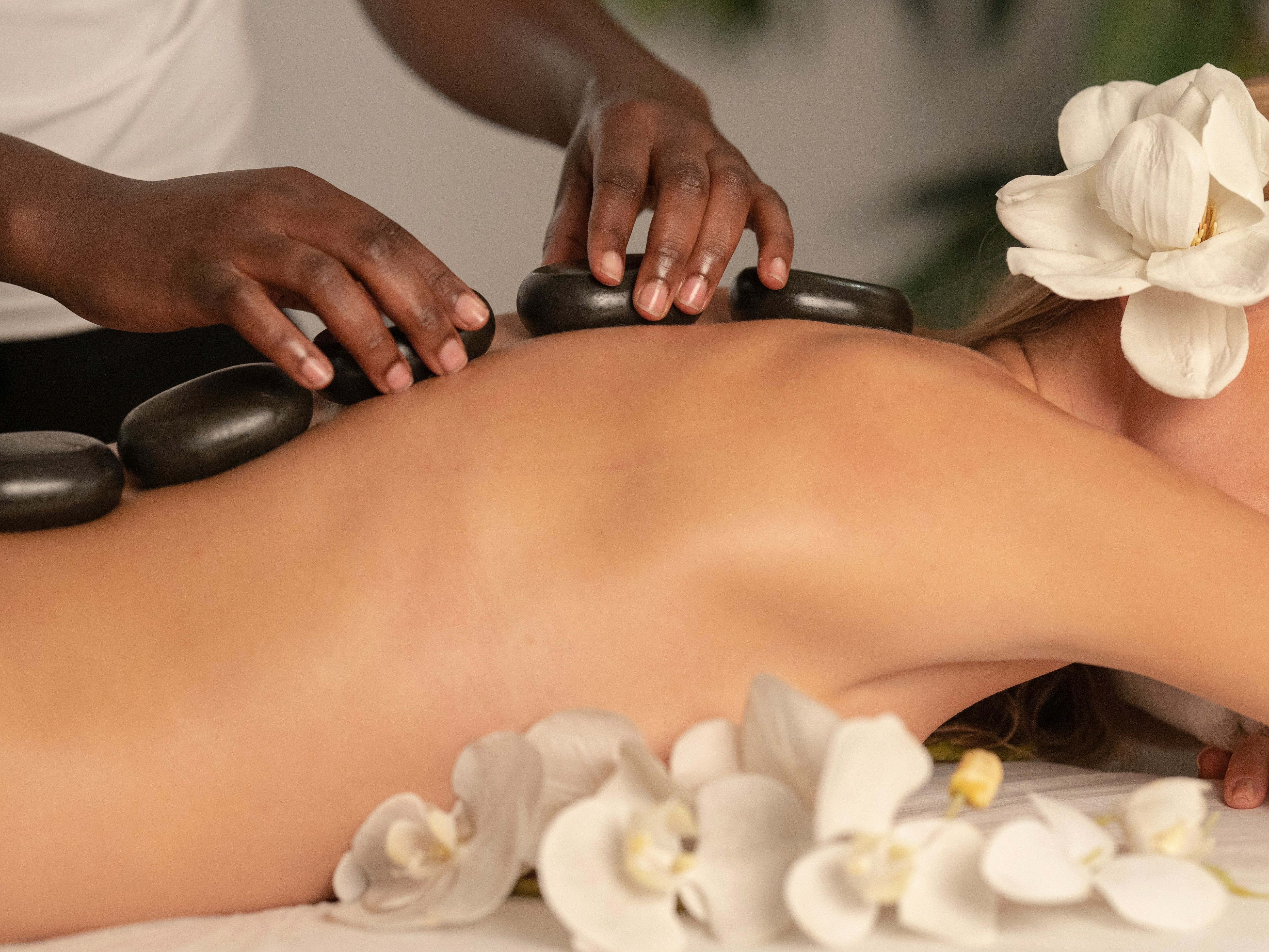 Person receiving a hot stone massage with white flowers around