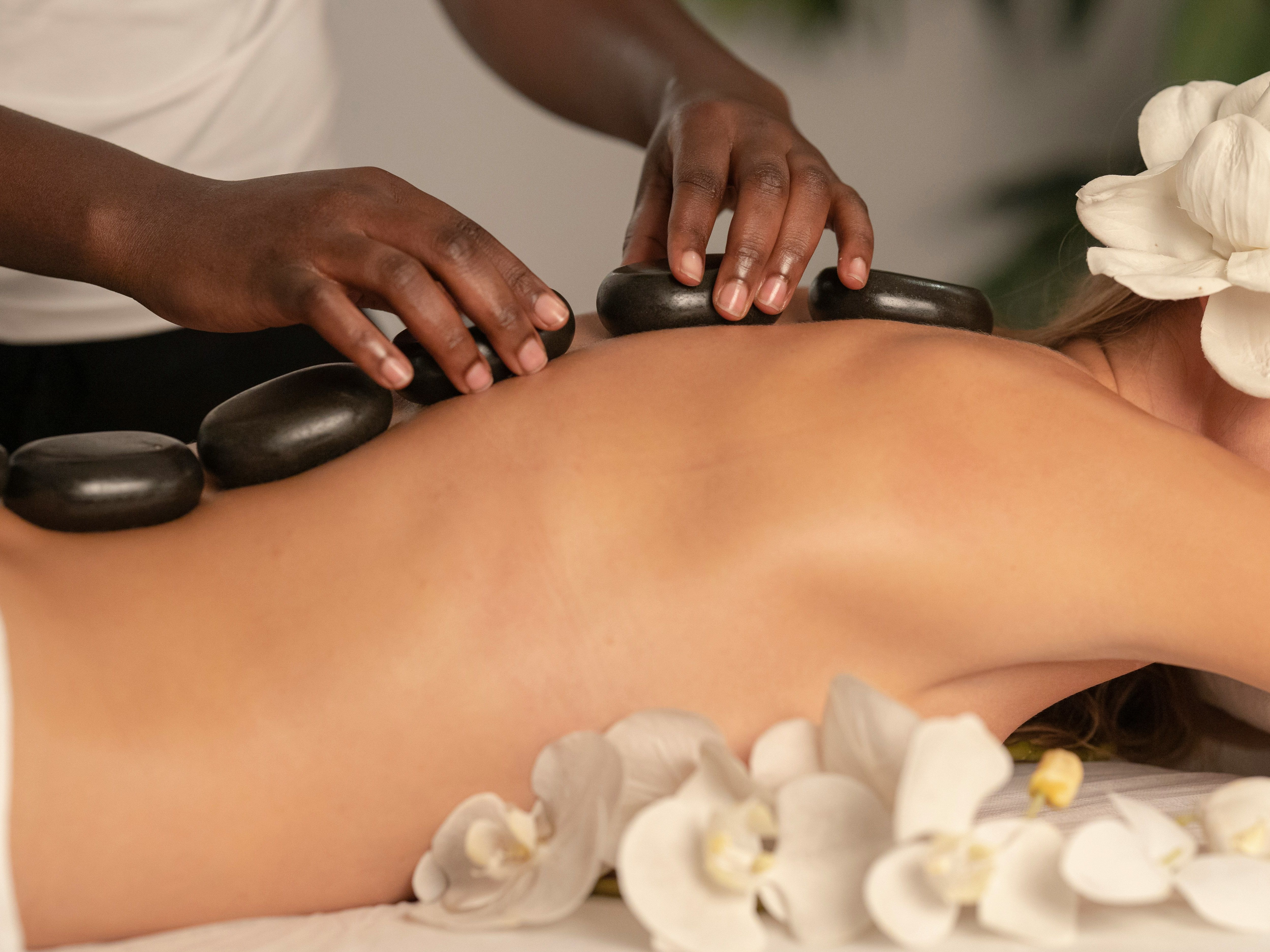 Person receiving a hot stone massage with white flowers around