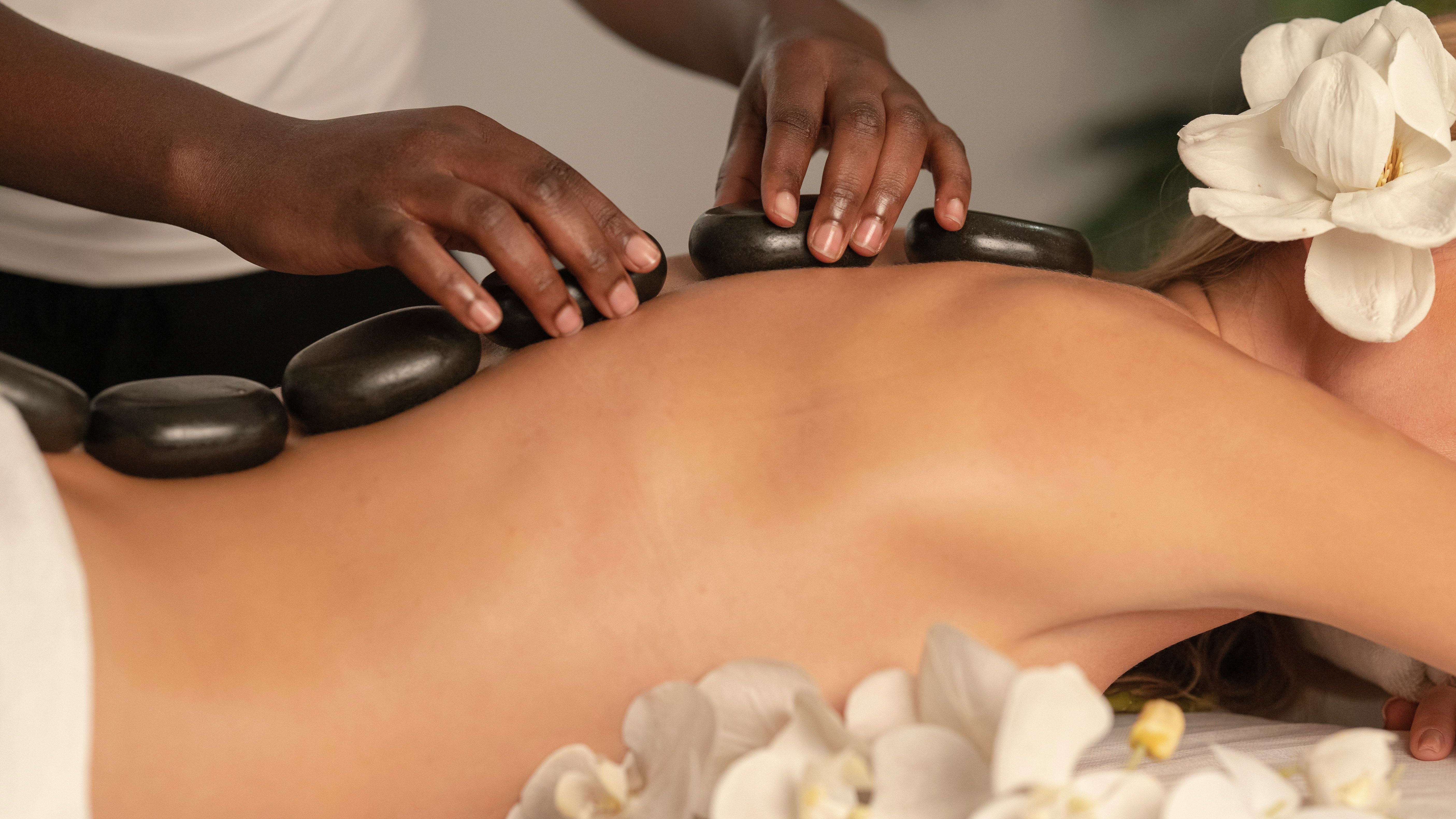 Person receiving a hot stone massage with white flowers around