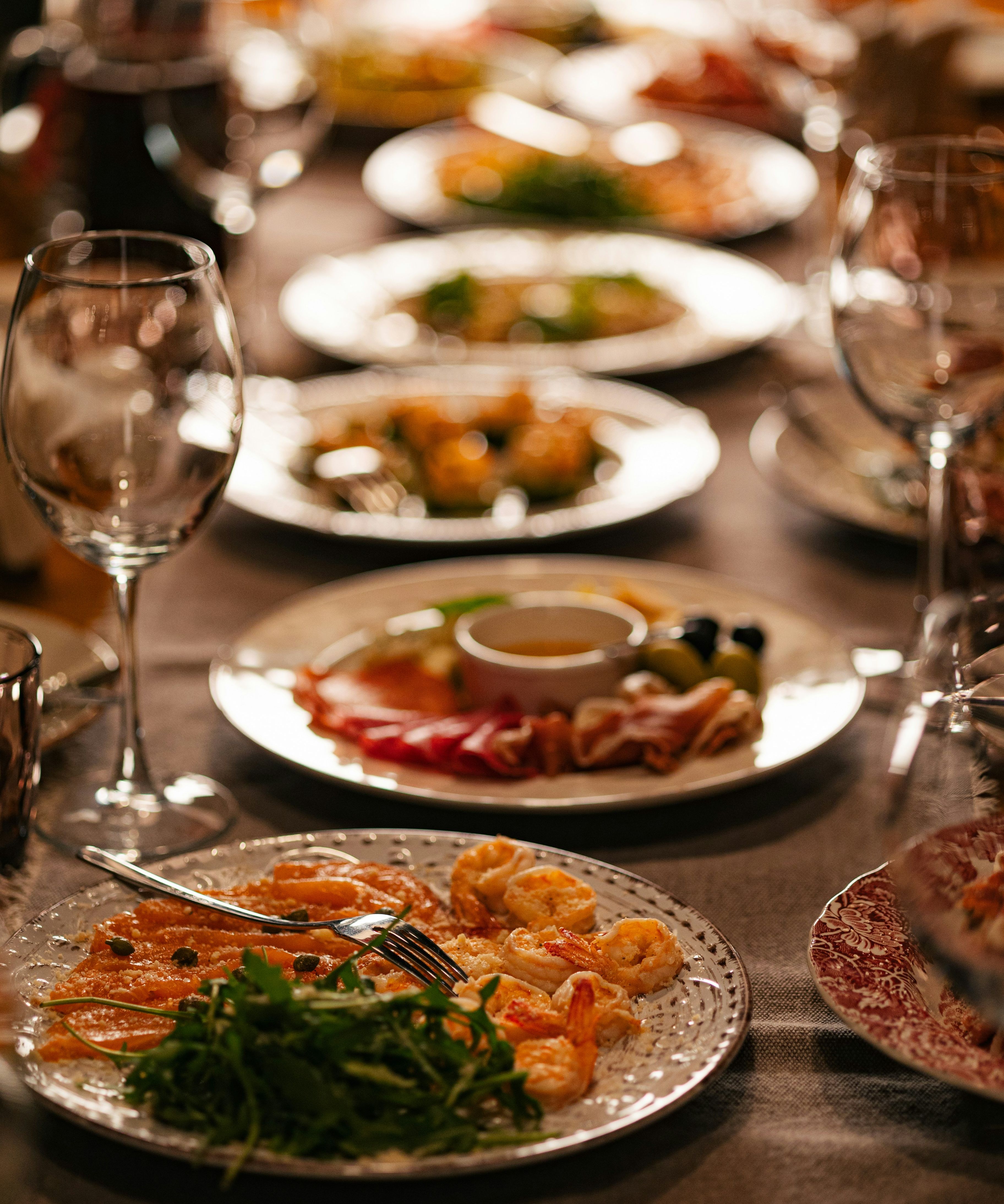 Elegant table setting with assorted plates of gourmet food and empty wine glasses
