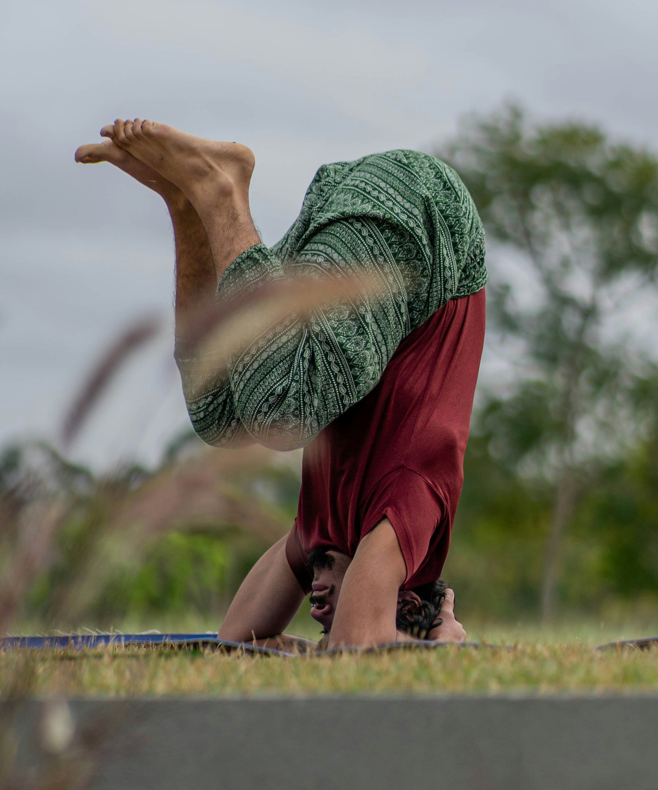 Person performing a headstand yoga pose outdoors on grass.