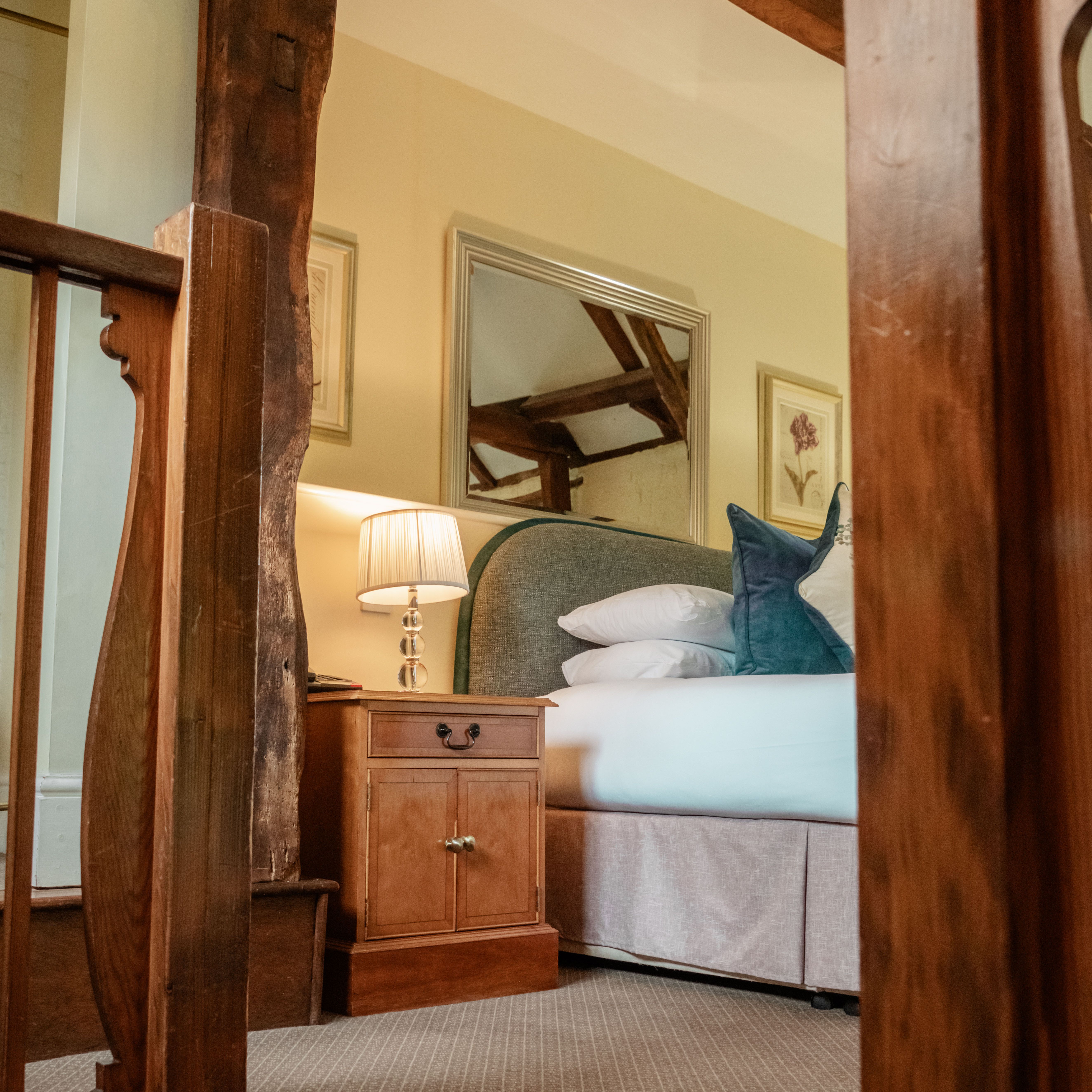 Cozy bedroom with a wooden nightstand, lamp, and a plush bed with pillows