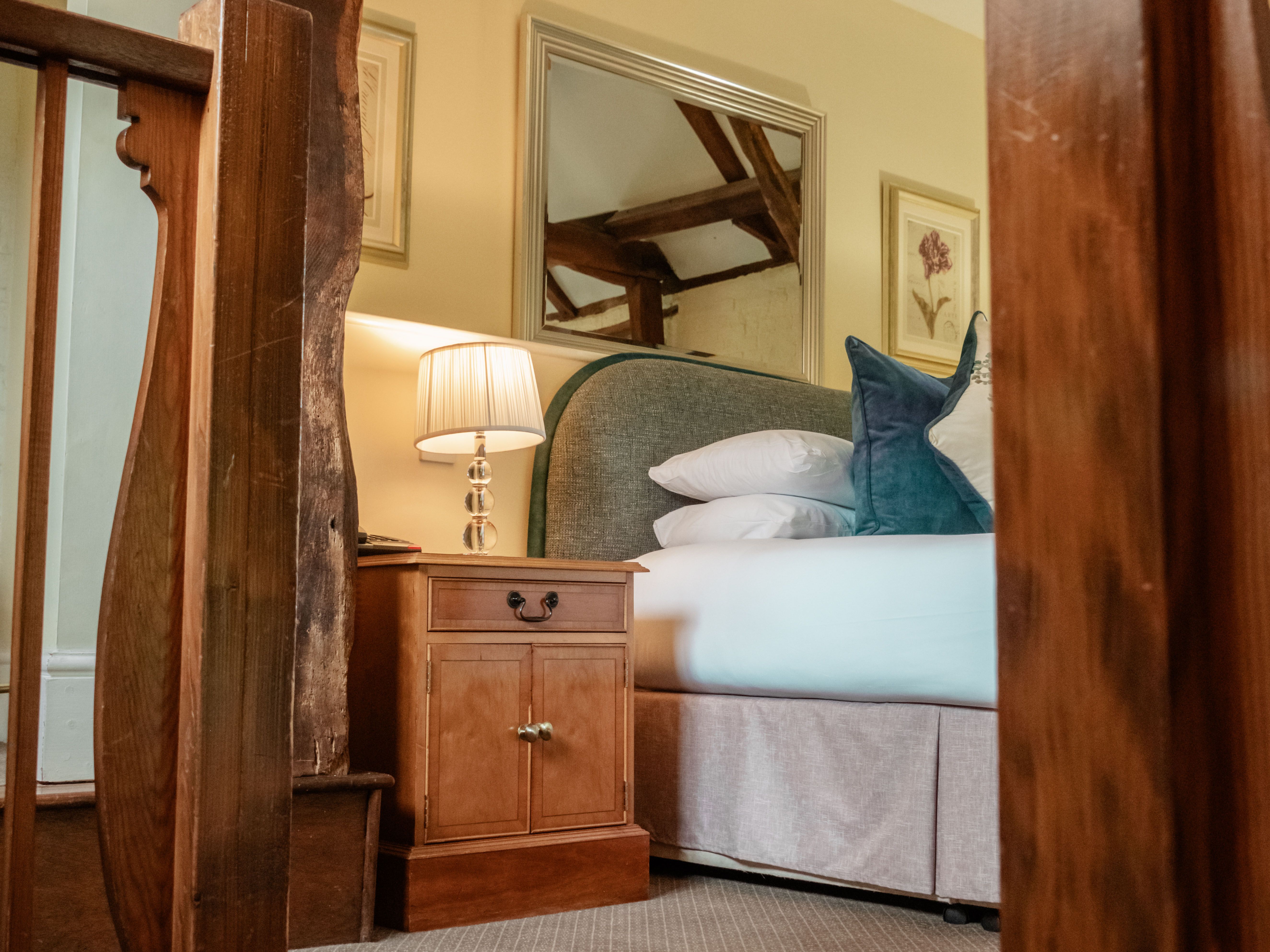 Cozy bedroom with a wooden nightstand, lamp, and a plush bed with pillows