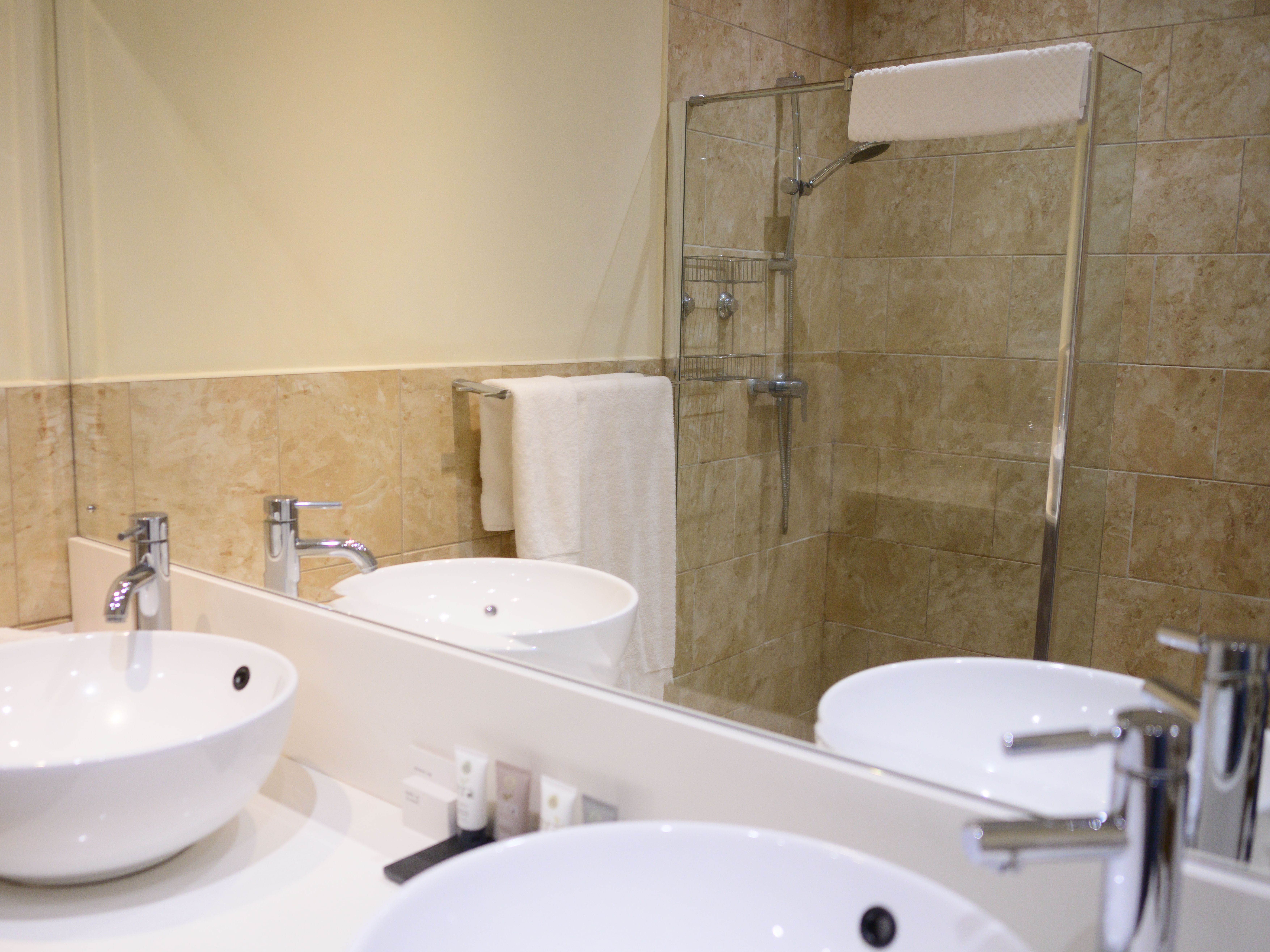 Modern bathroom with white vessel sinks, large mirror, and a glass-enclosed shower