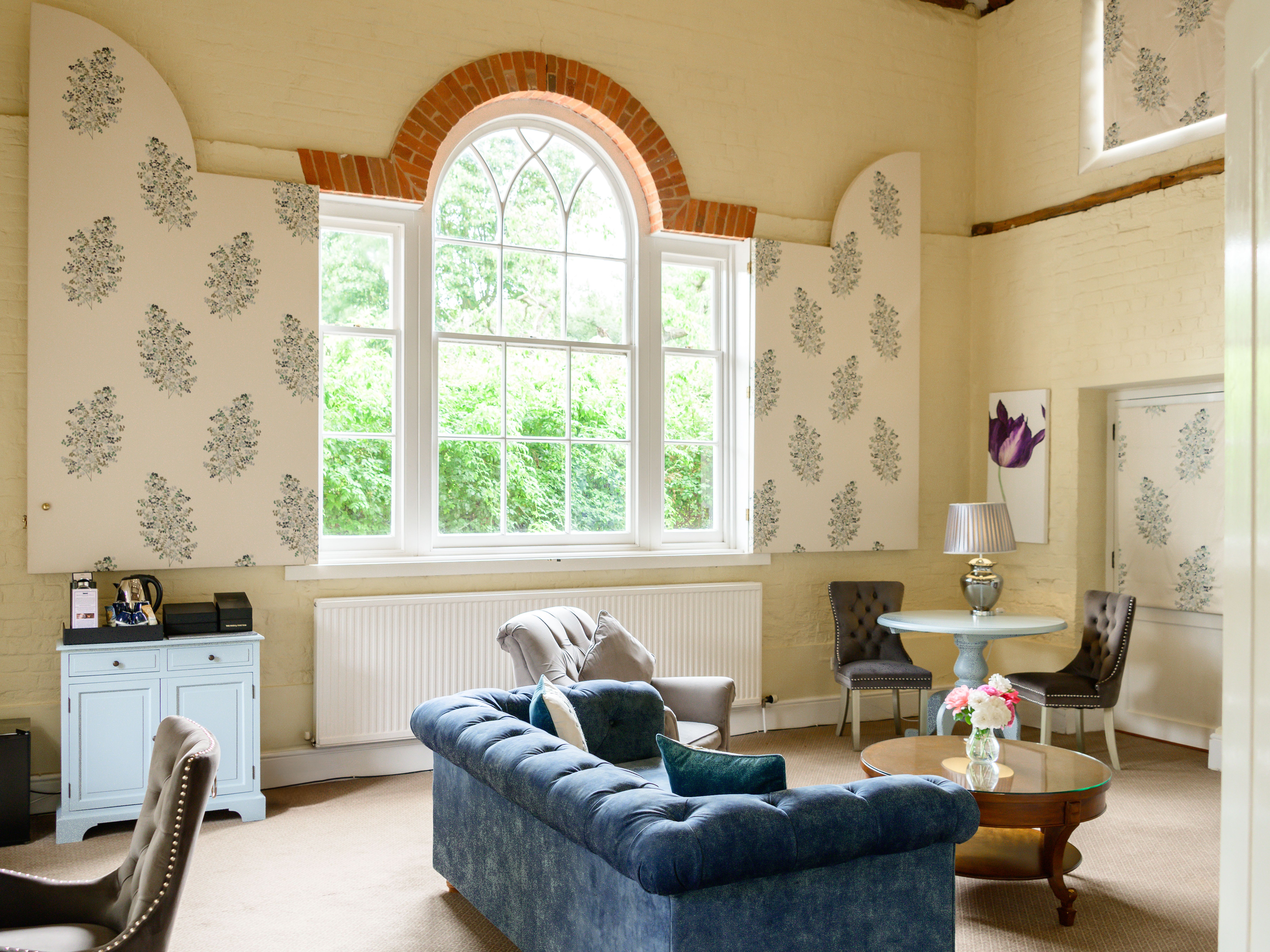 Elegant living room with vintage furniture, large arched window, and floral wallpaper panels